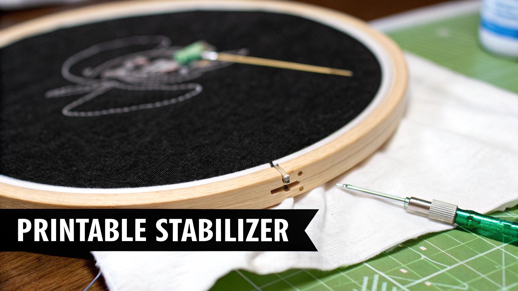 A close-up of an embroidery hoop with a white design on black fabric, a punch needle tool, and 'Printable Stabilizer' text.