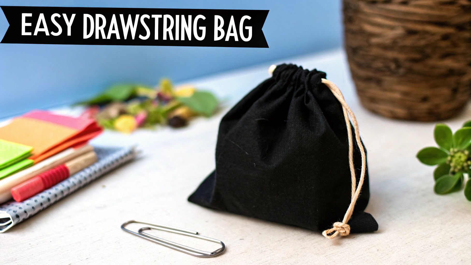 A black drawstring bag with a beige string on a white table, surrounded by crafting supplies.