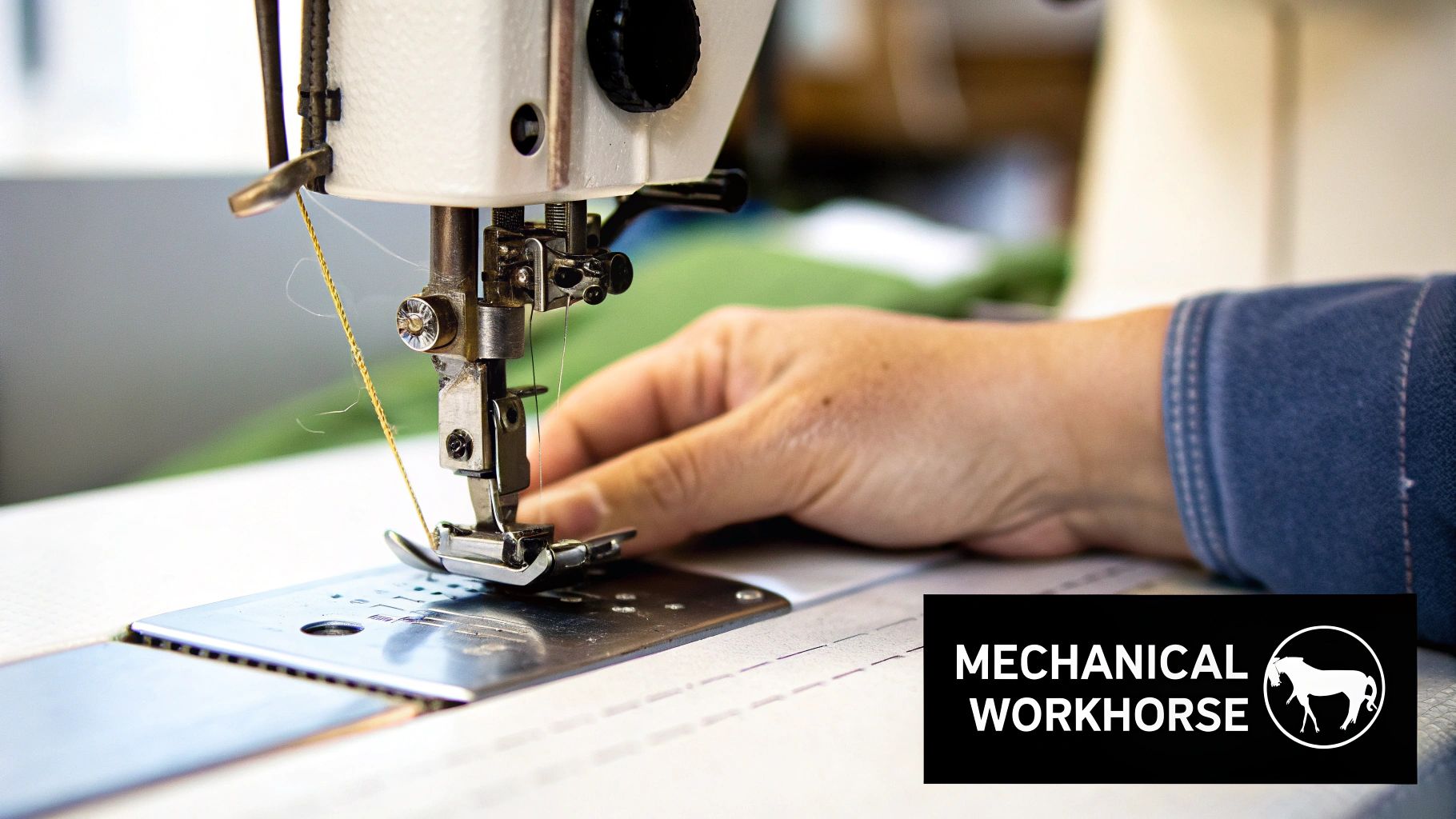 Close-up of a person's hand guiding fabric on a mechanical industrial sewing machine with yellow thread.