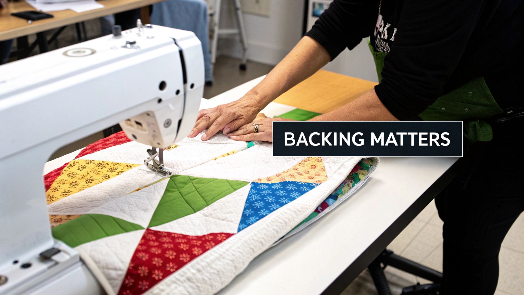 A person's hands guiding a colorful quilt under the needle of a white sewing machine.