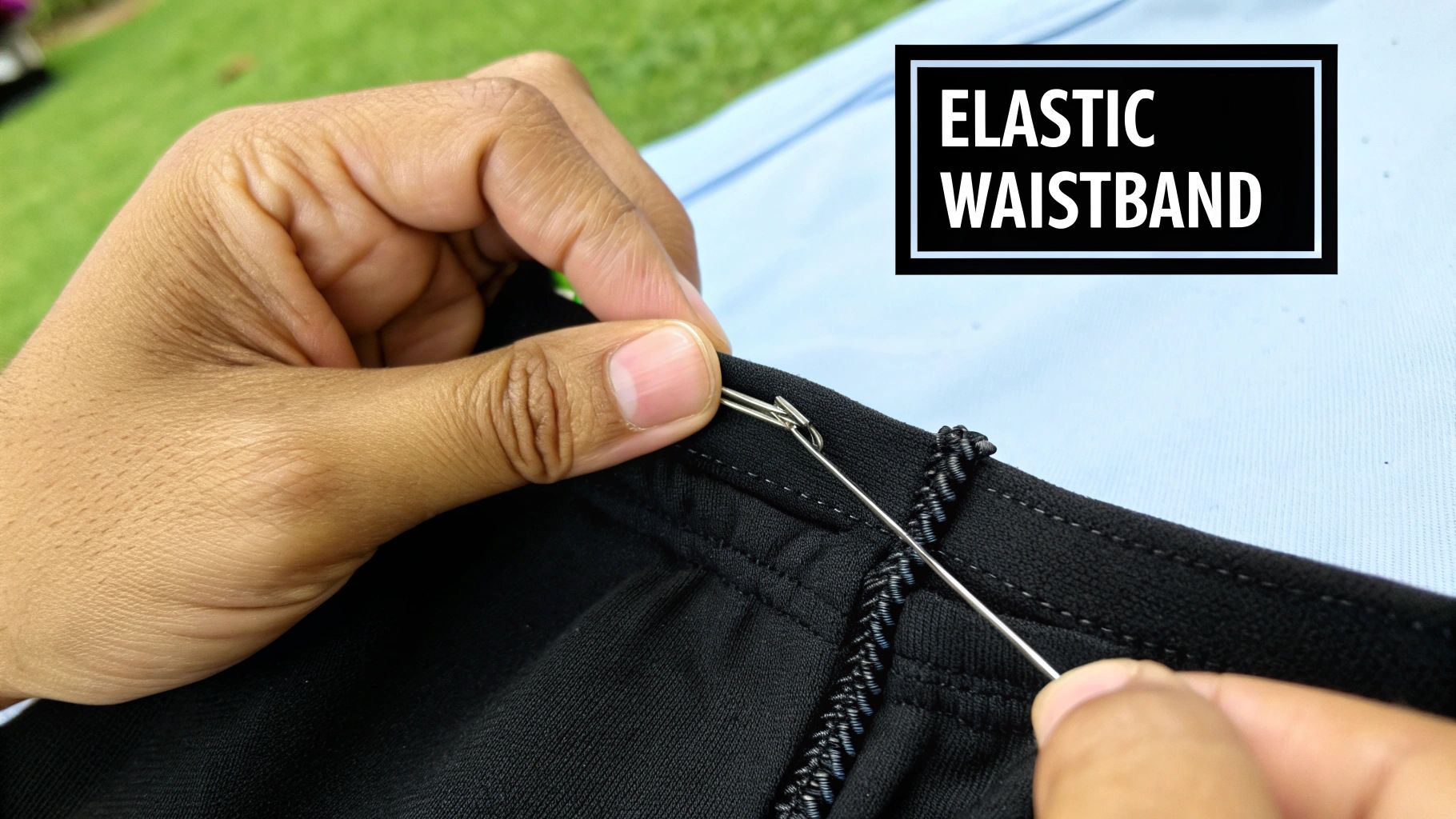 Close-up of hands using a safety pin to thread elastic into a black fabric waistband with 'ELASTIC WAISTBAND' text.