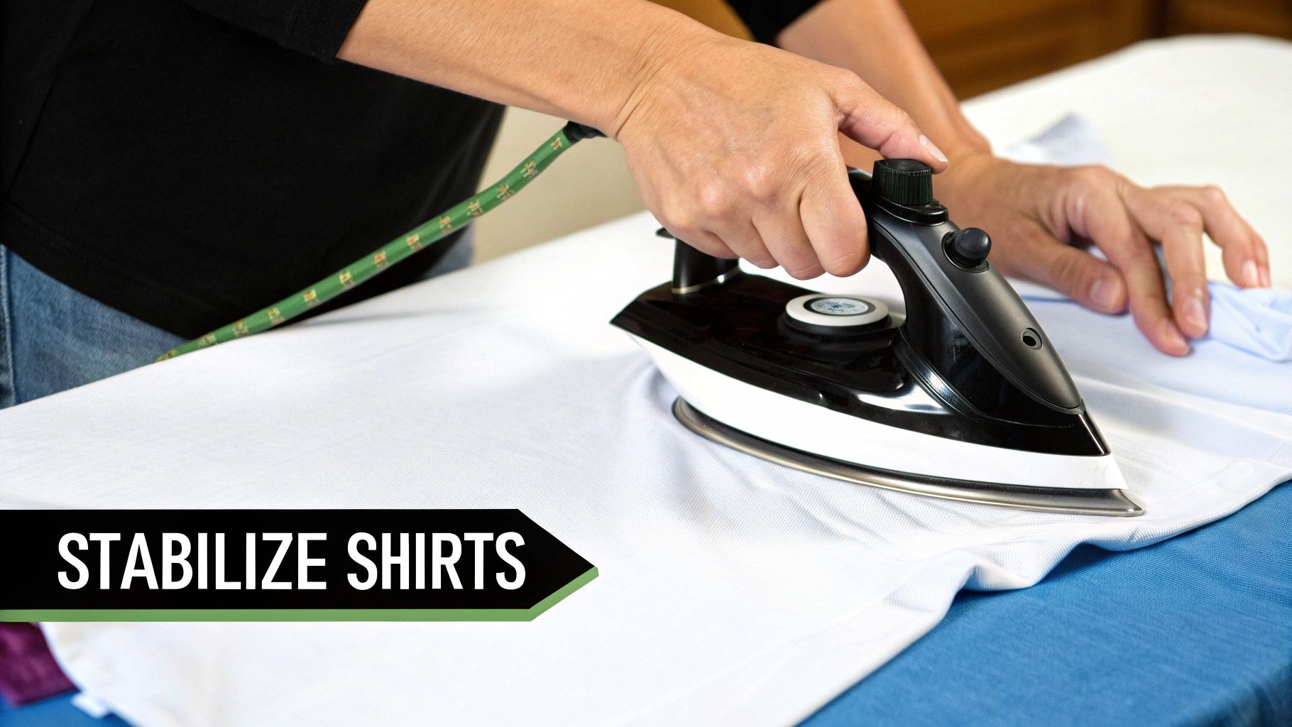 A person's hands are seen ironing a white t-shirt on an ironing board with a black iron.