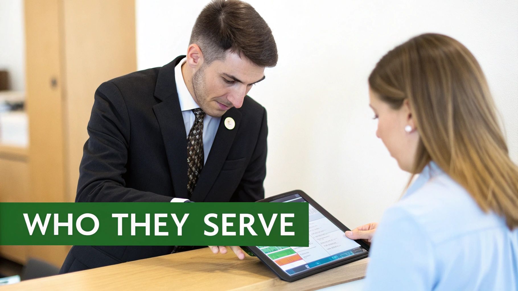 A man in a suit helps a woman review information on a tablet in a professional setting.