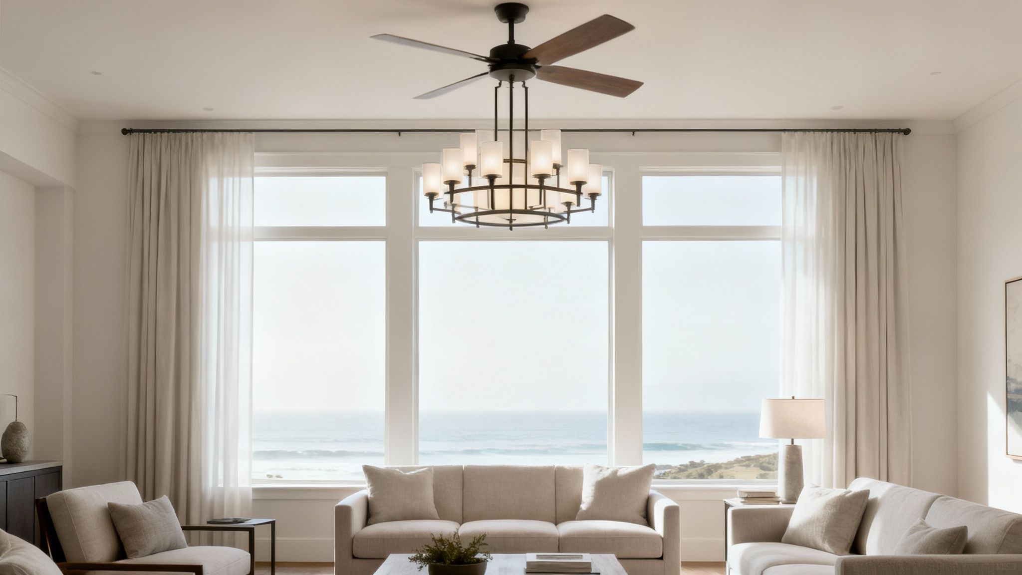 A spacious living room featuring a ceiling fan with chandelier, cream sofas, and large windows with ocean views.