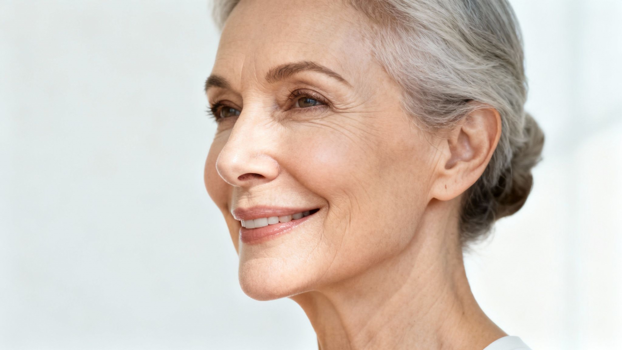 Close-up side profile of a smiling senior woman with elegant grey hair.