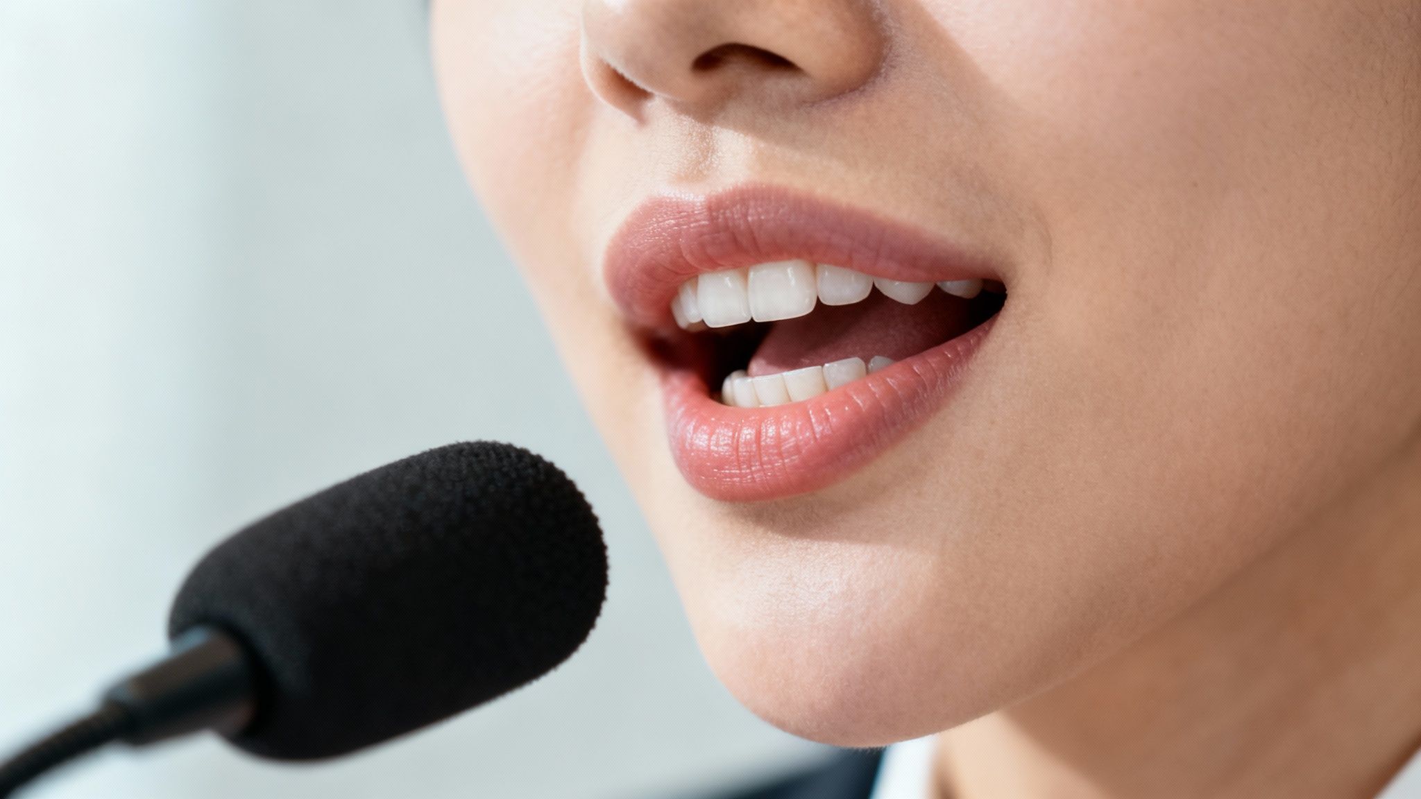 Close-up of a person speaking into a black microphone with their mouth open, showing white teeth.