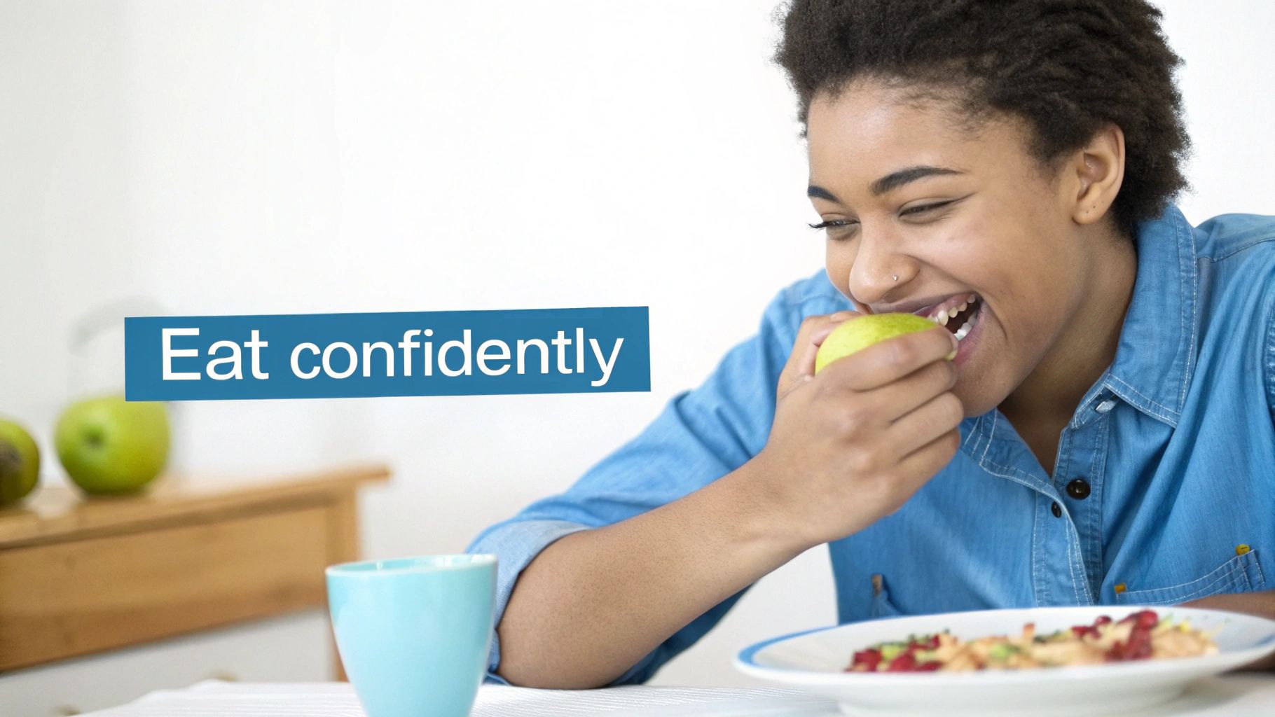 A smiling young woman confidently eats a green apple with a plate of food.