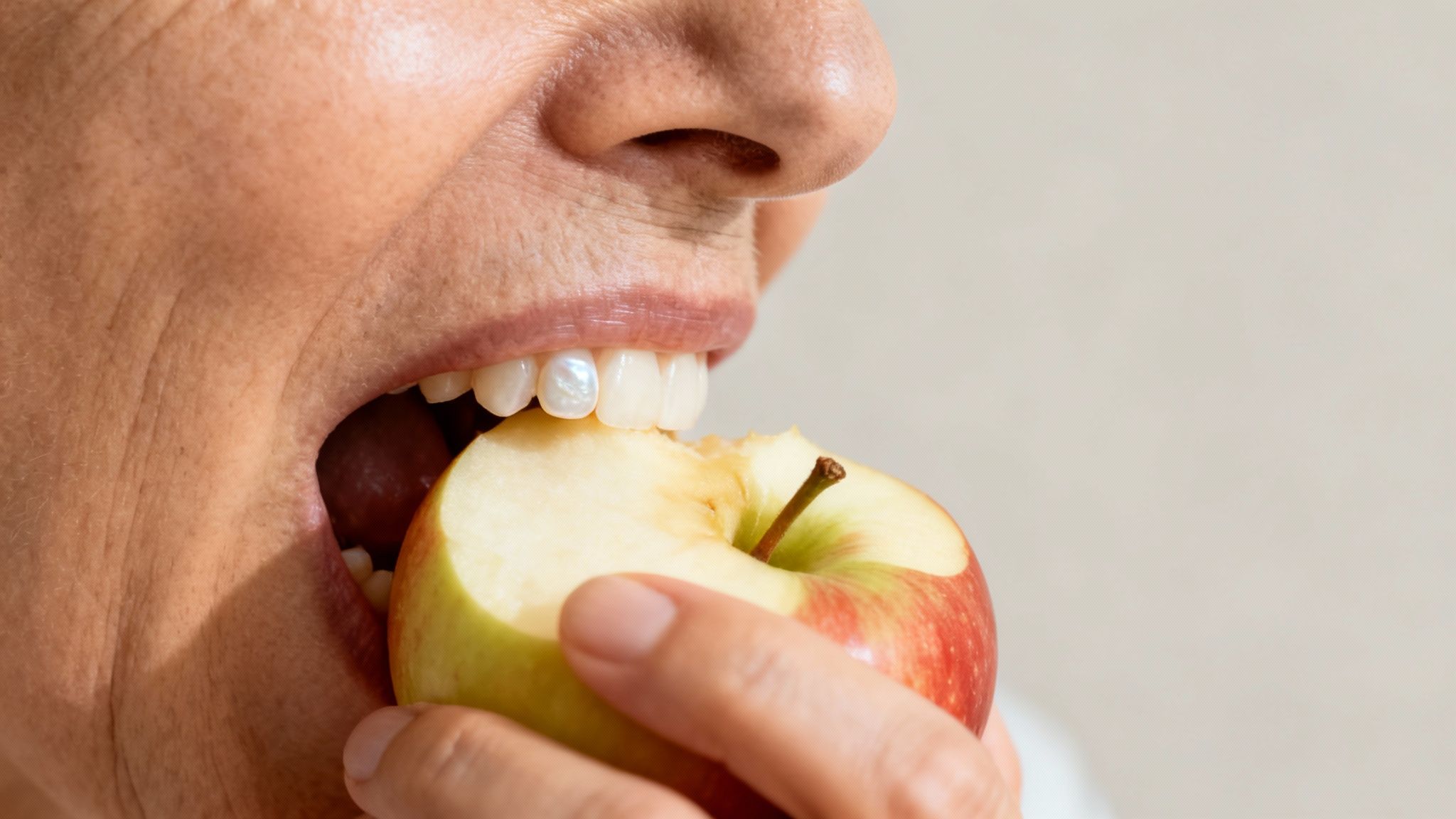 Close-up of a person with a dental crown on a front tooth biting into an apple.