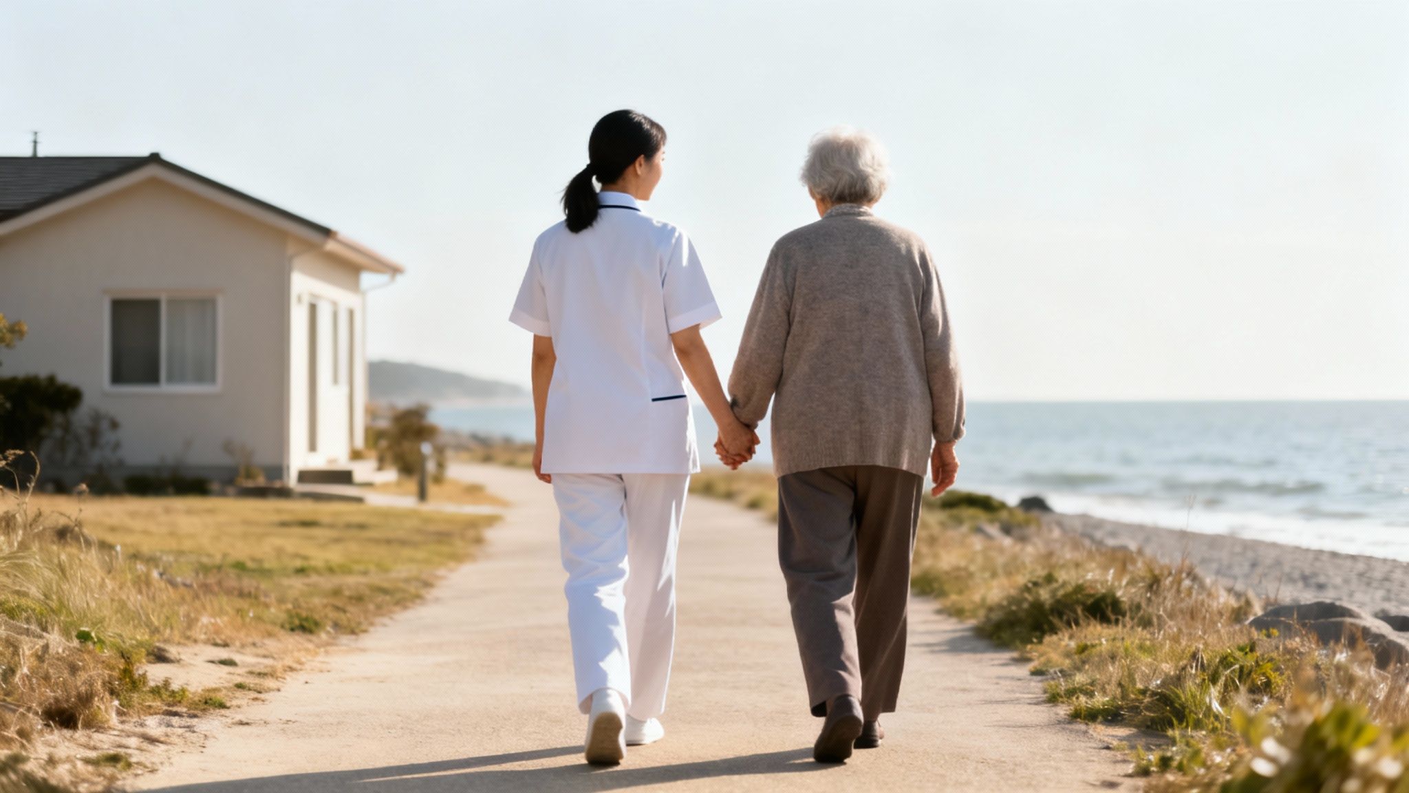 A caring nurse assists an elderly woman, walking hand-in-hand along a scenic coastal path.