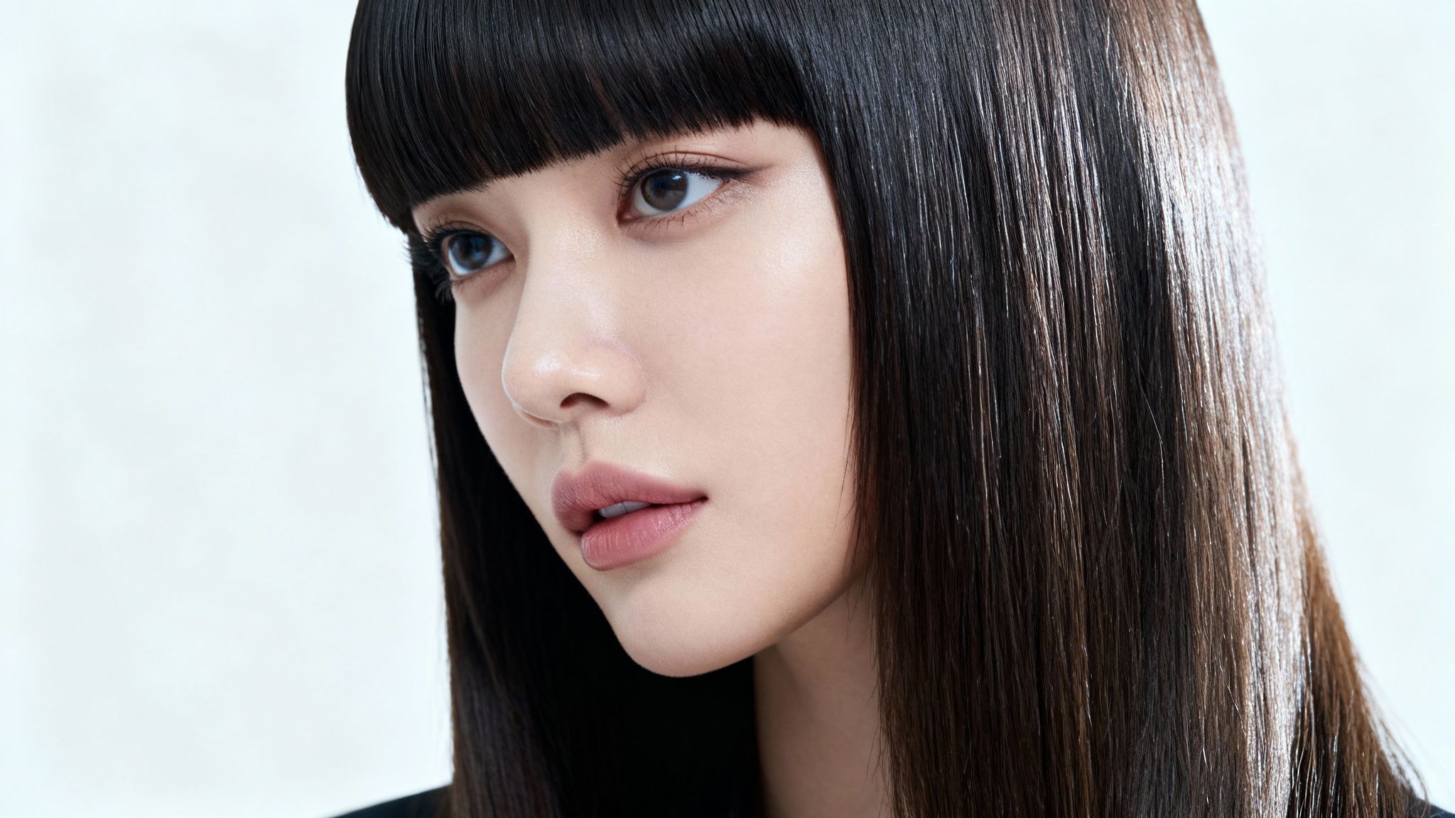 Primer plano de una mujer con cabello liso y oscuro, flequillo recto y maquillaje natural.