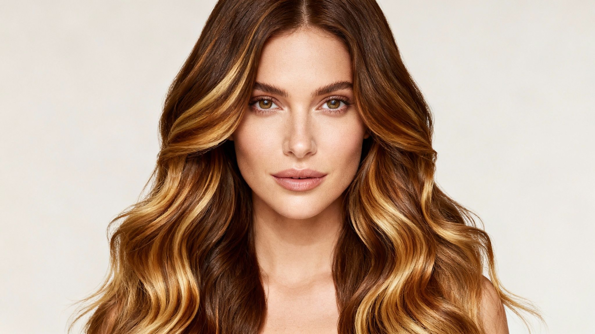 Primer plano de una mujer sonriendo con cabello castaño largo y ondulado con mechas rubias.