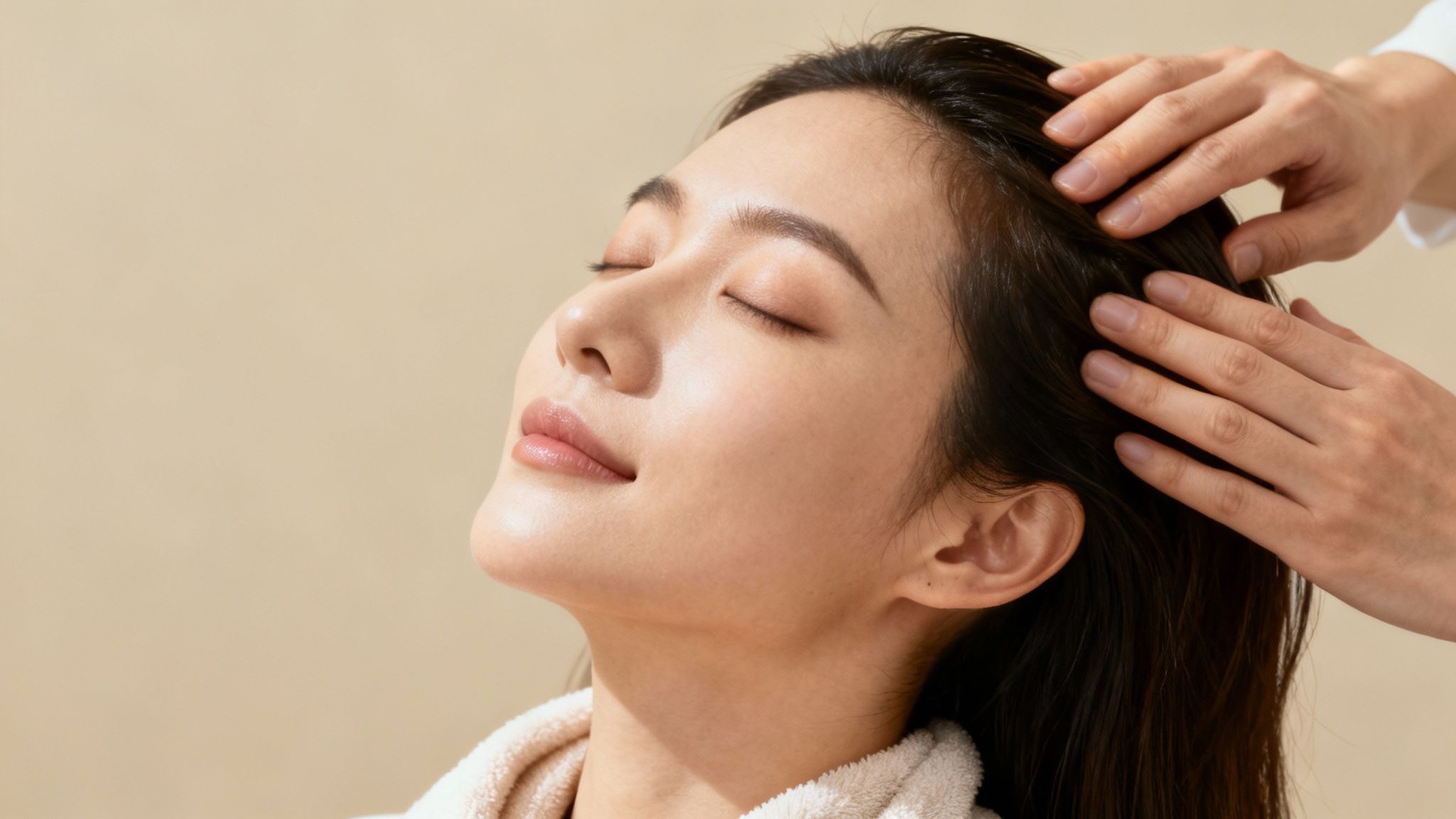 Mujer asiática relajándose con un masaje capilar profesional, ojos cerrados y expresión serena.