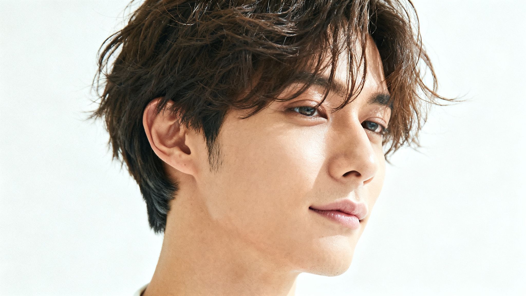 Primer plano de un hombre asiático joven con cabello oscuro, ondulado y una expresión suave.