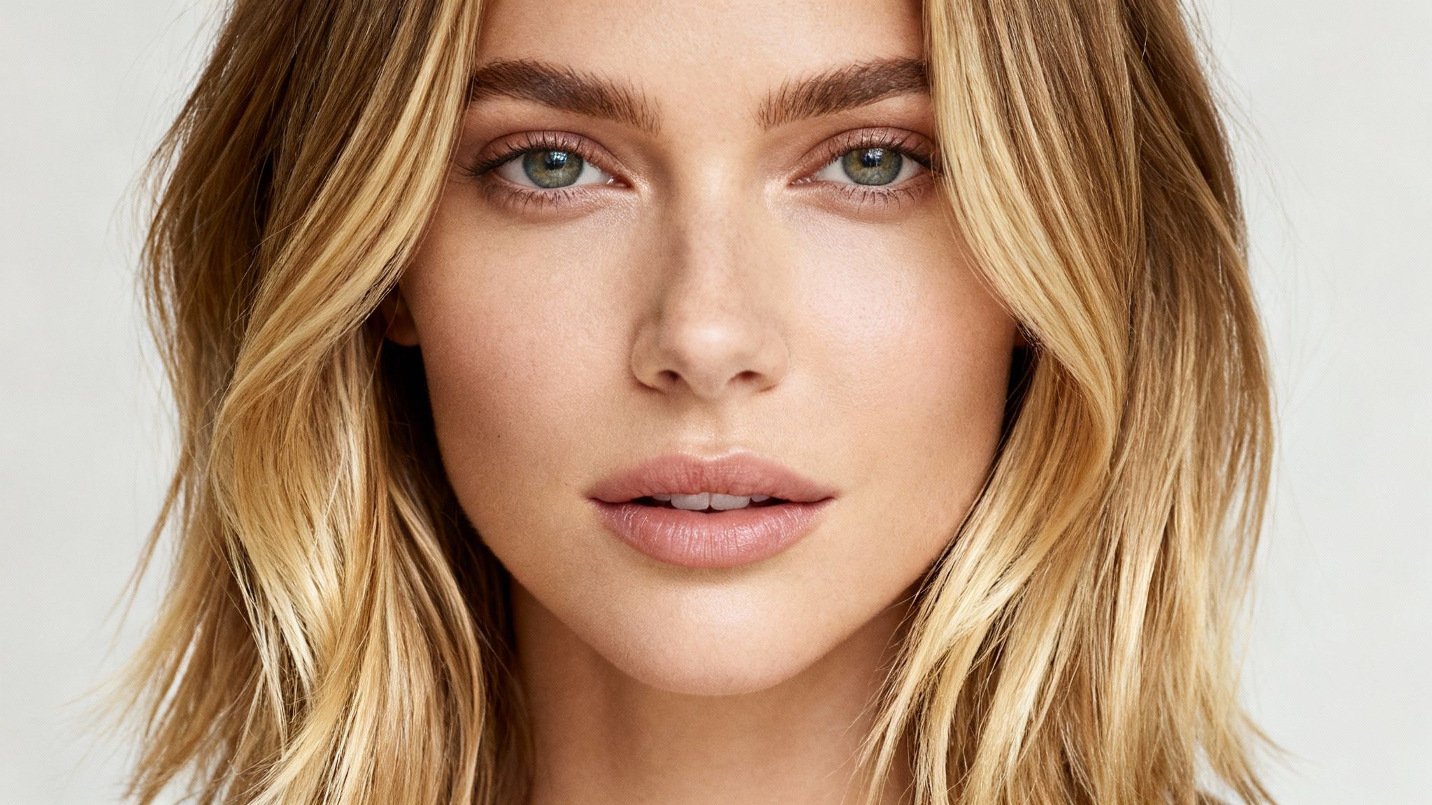 Primer plano de una mujer rubia con cabello ondulado y ojos verdes, mirando directamente a la cámara.