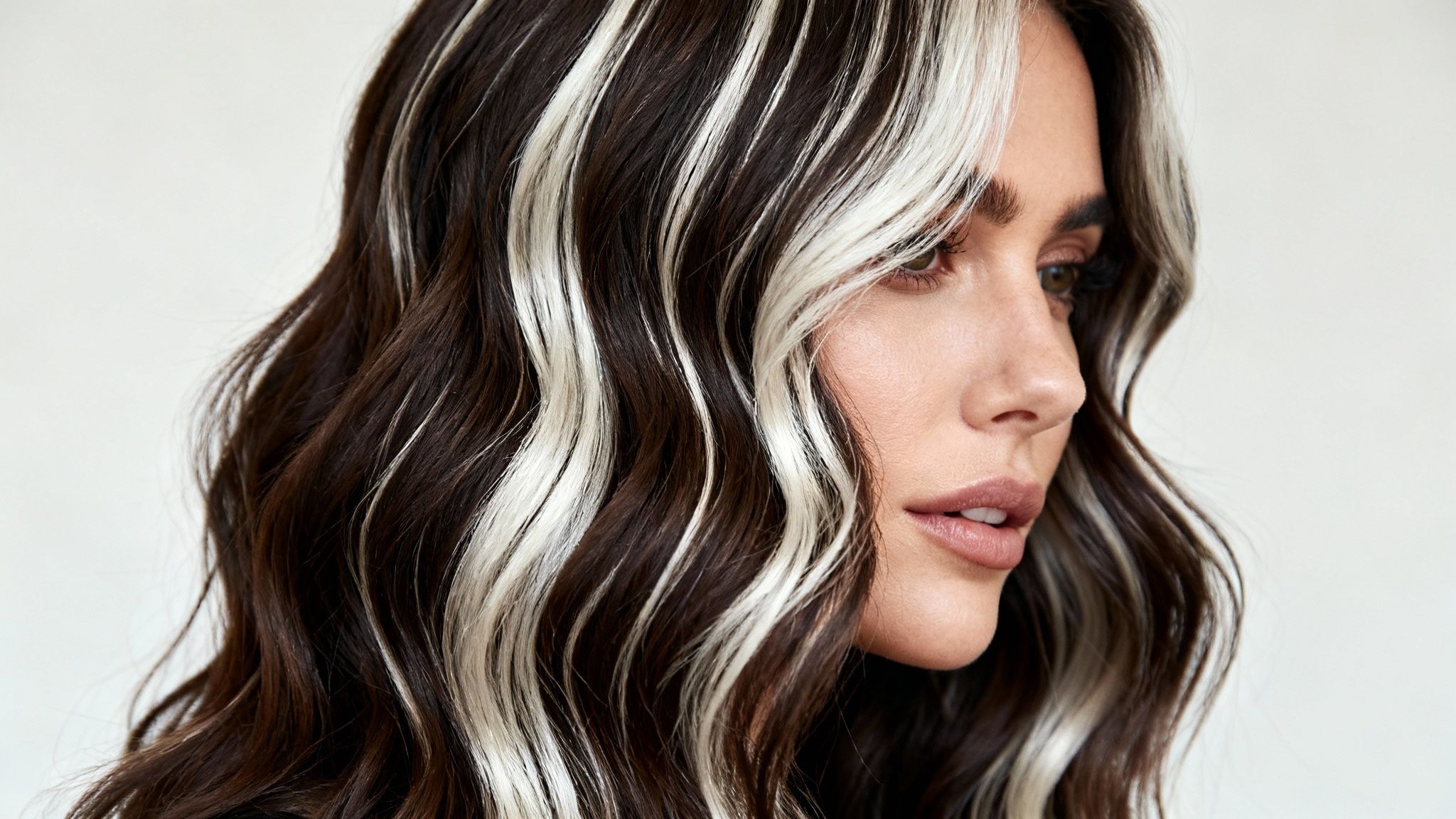 Mujer con cabello castaño oscuro y mechas balayage rubias platinadas estilo chunky highlights