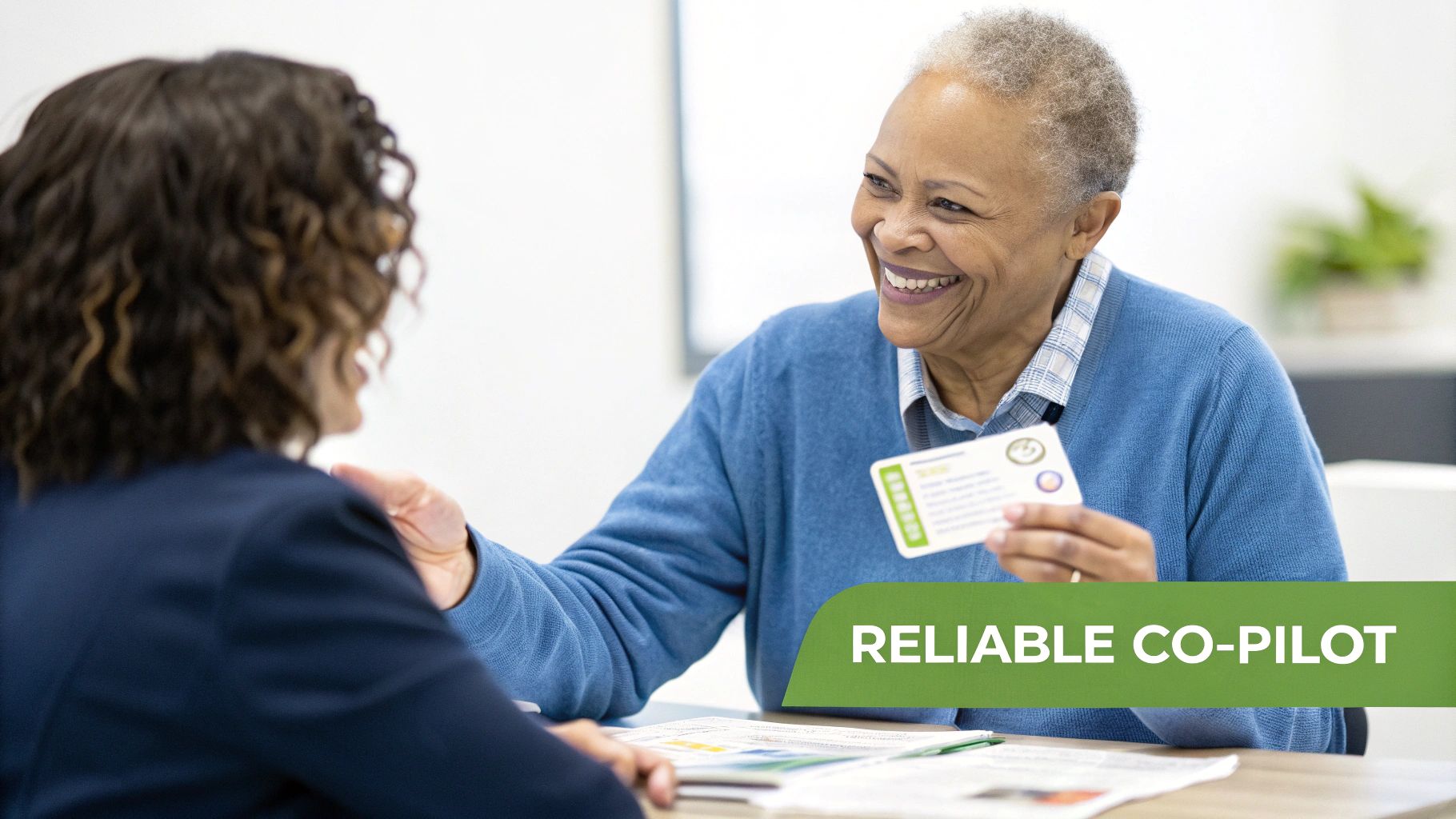 A happy senior Black woman shows a card to a person, likely receiving Medicare advice.