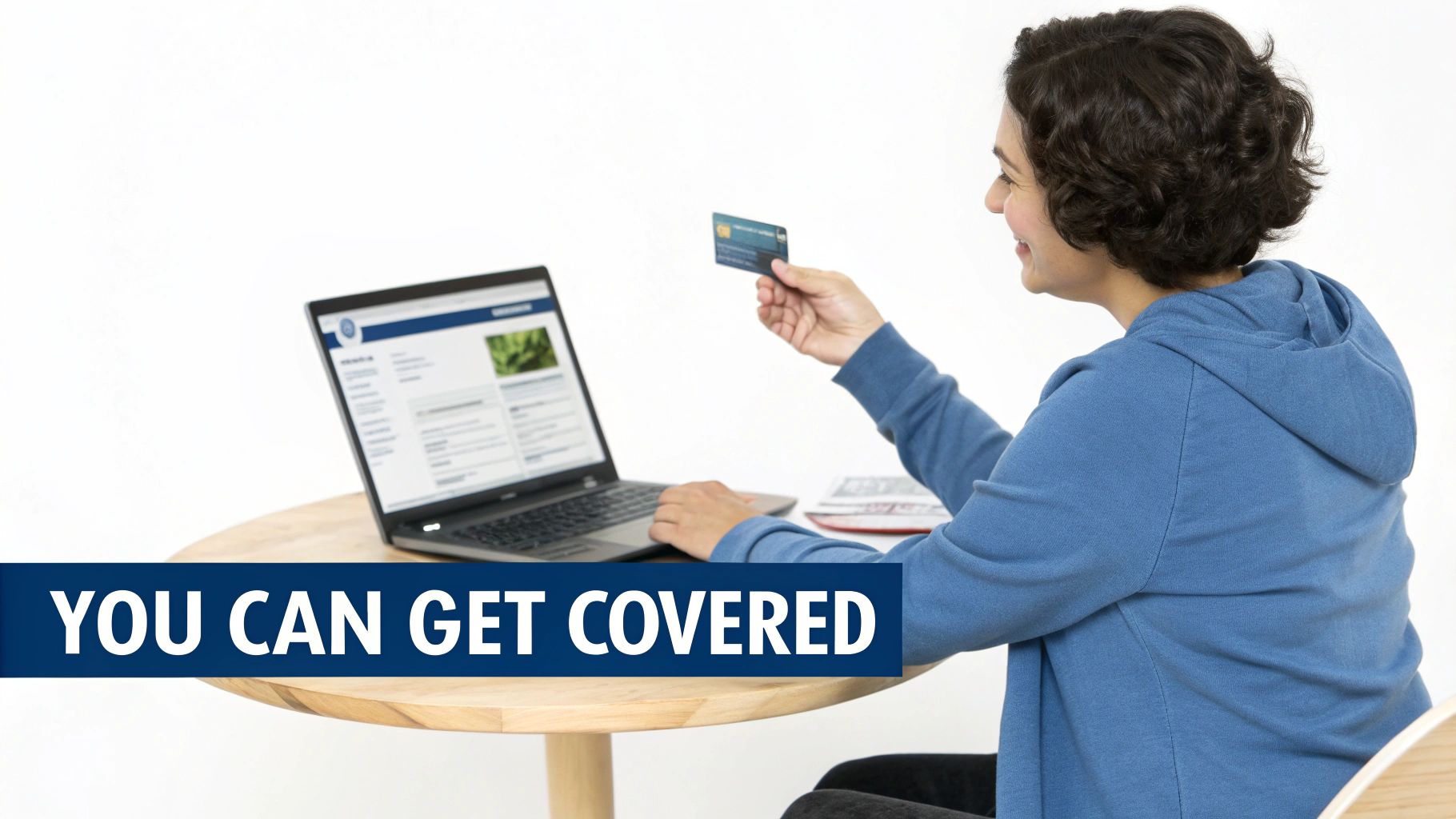 A person in a blue hoodie uses a laptop and holds a credit card, emphasizing online coverage.