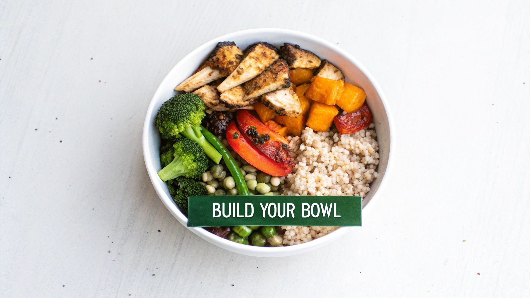 A colorful, healthy build-your-own bowl with grilled chicken, broccoli, sweet potato, grains, and roasted tomato.