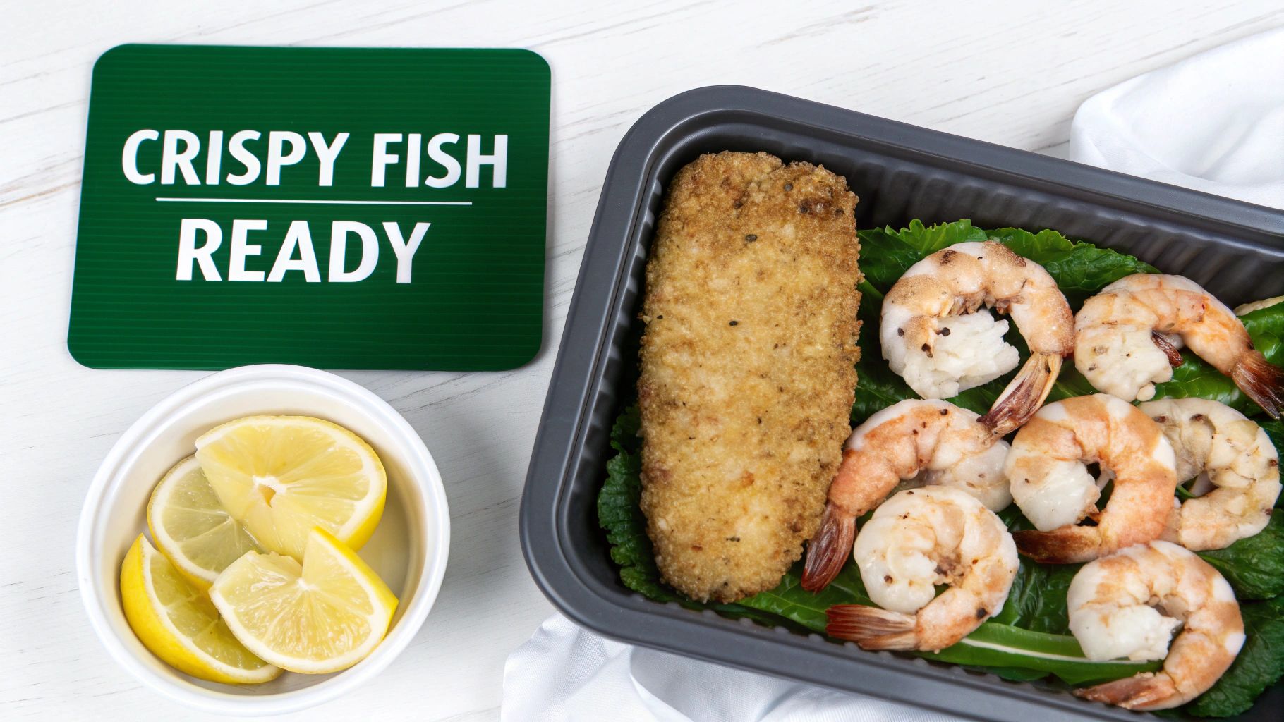 Breaded fish fillet and seasoned shrimp on bed of lettuce with lemon slices in meal prep container