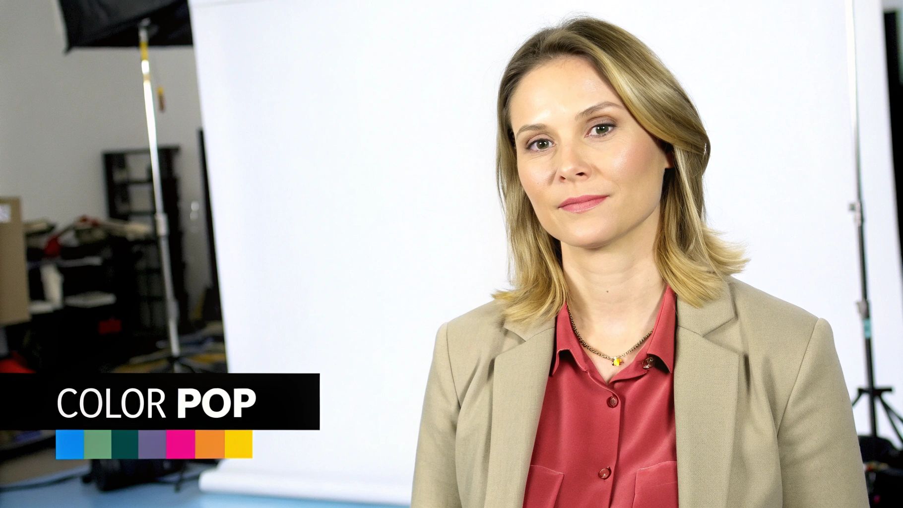 A blonde woman in a red blouse and beige blazer poses for a studio portrait.