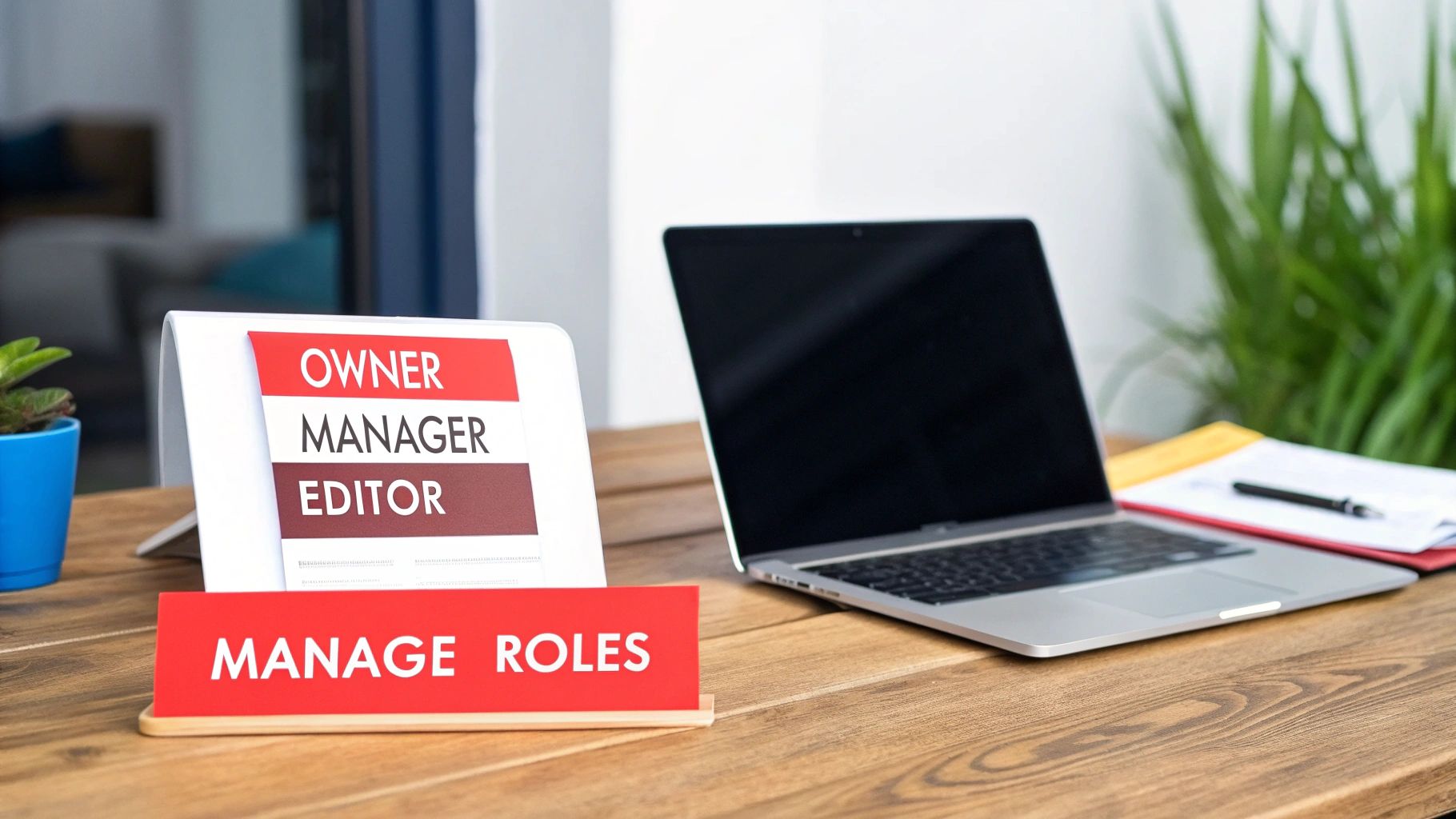A desk with a sign showing 'Owner', 'Manager', 'Editor', and 'Manage Roles', beside an open laptop.