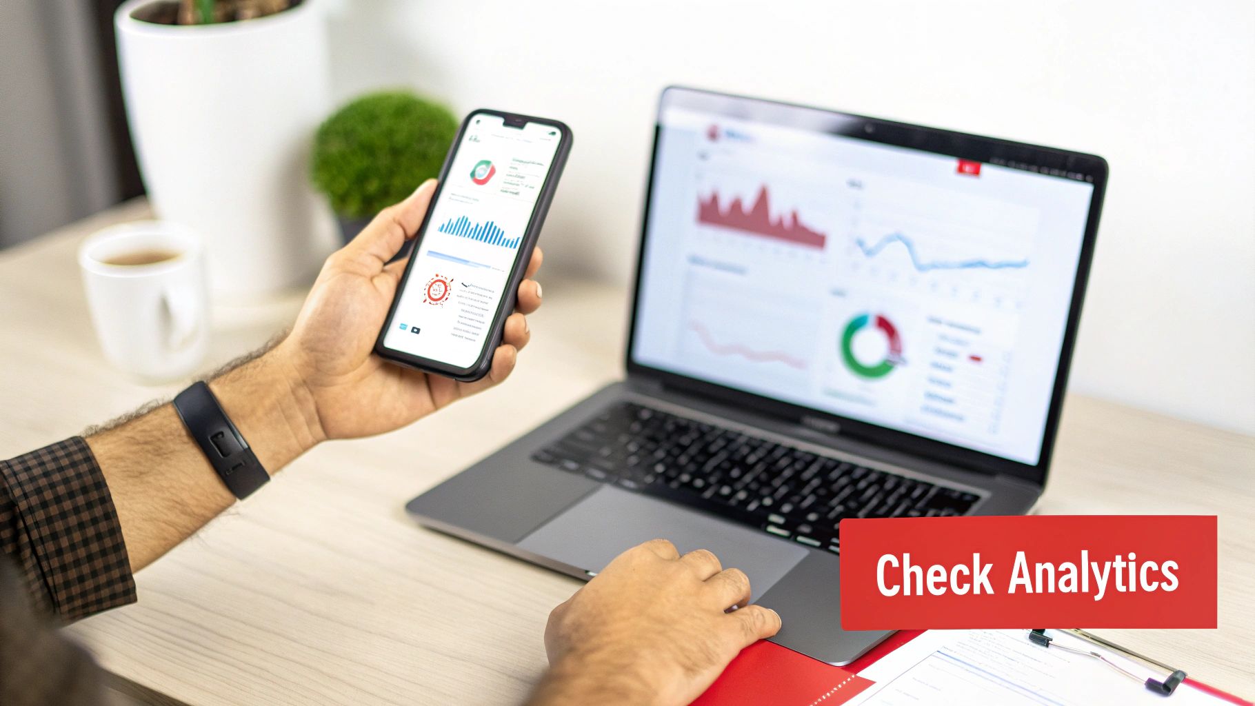 Hands hold a smartphone and use a laptop, both displaying business analytics charts and graphs.