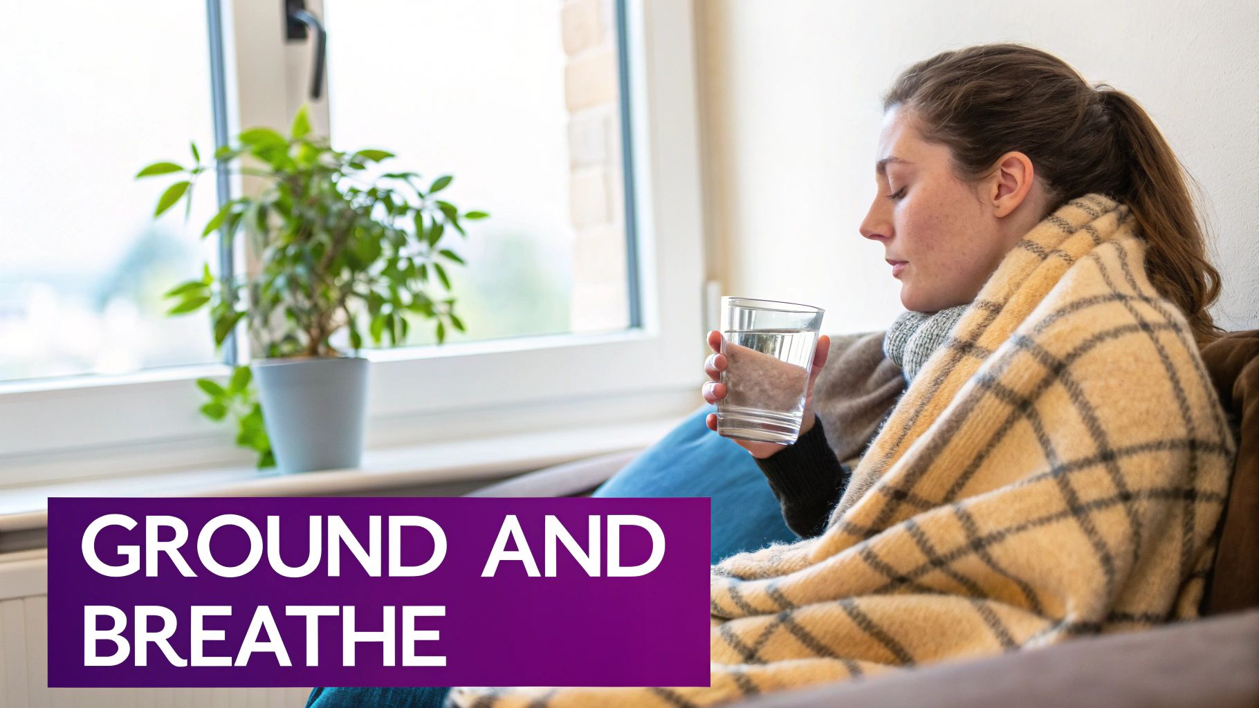 A woman wrapped in a blanket, holding water, with her eyes closed, grounding herself.