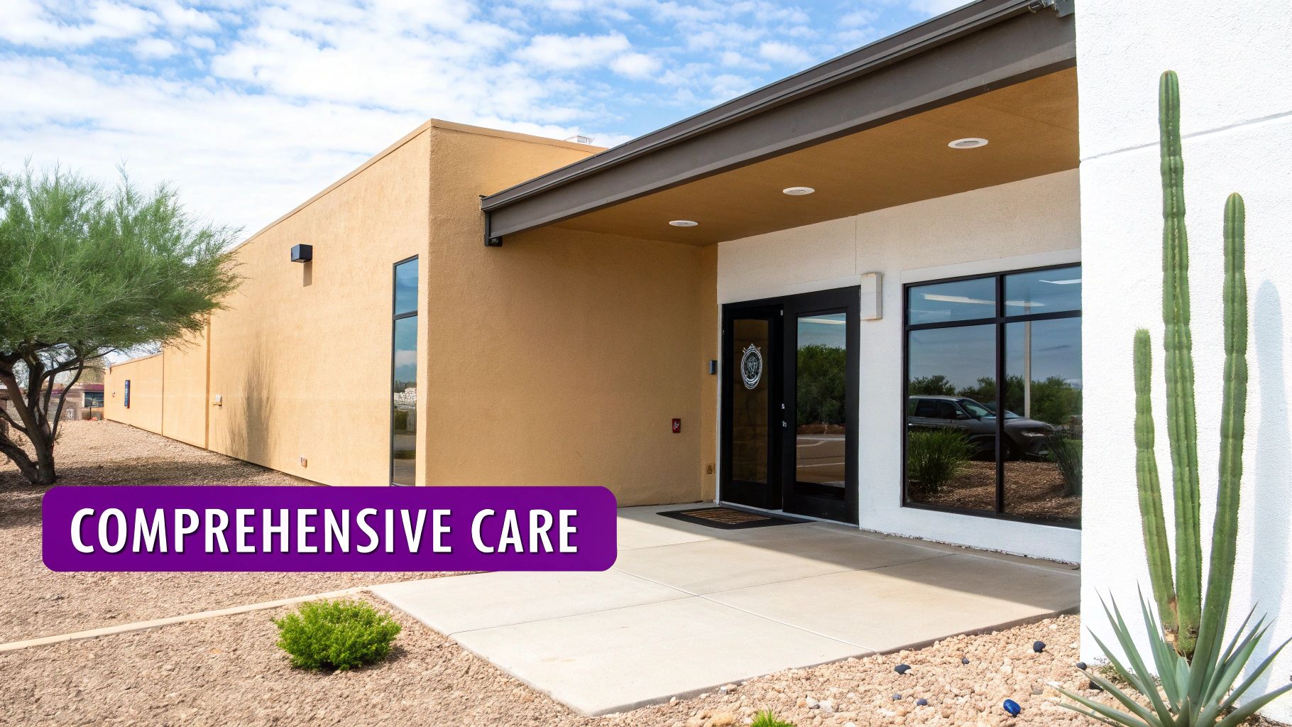 A modern desert building with tan and white walls, an inviting entrance, and desert landscaping, featuring a banner saying 'COMPREHENSIVE CARE'.