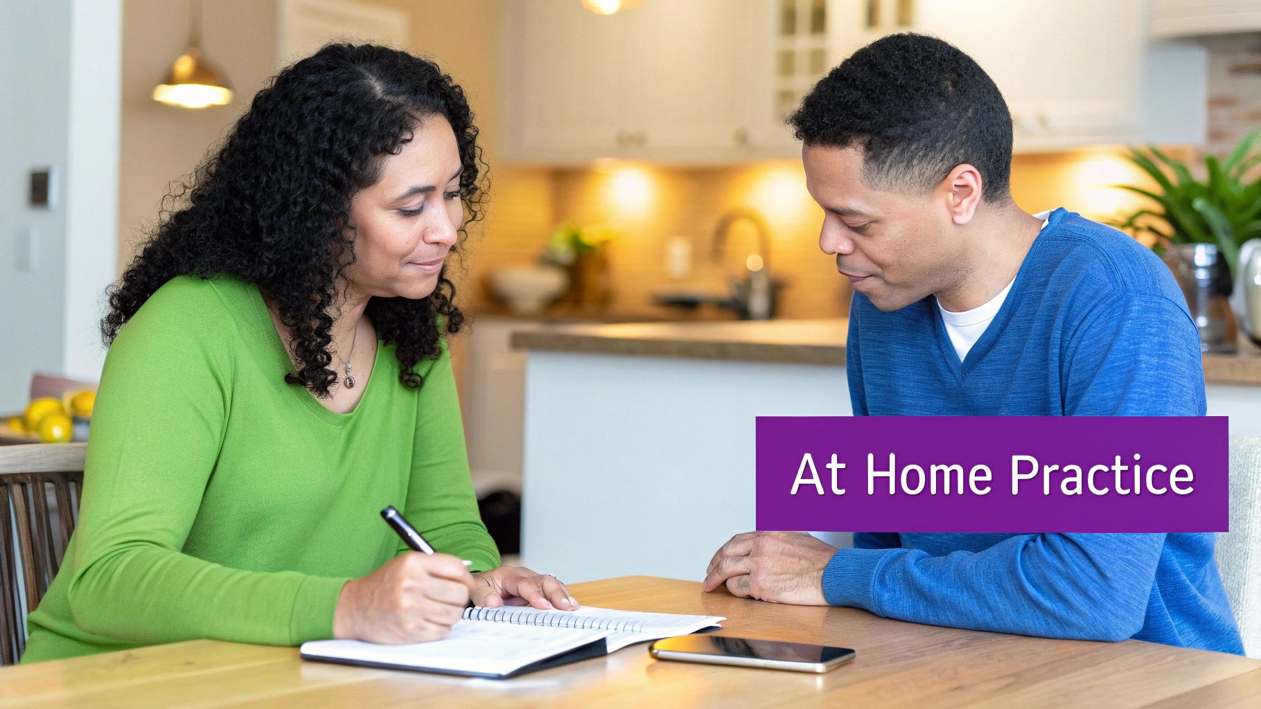 A man and a woman sitting at a table, focused on writing in a notebook at home.