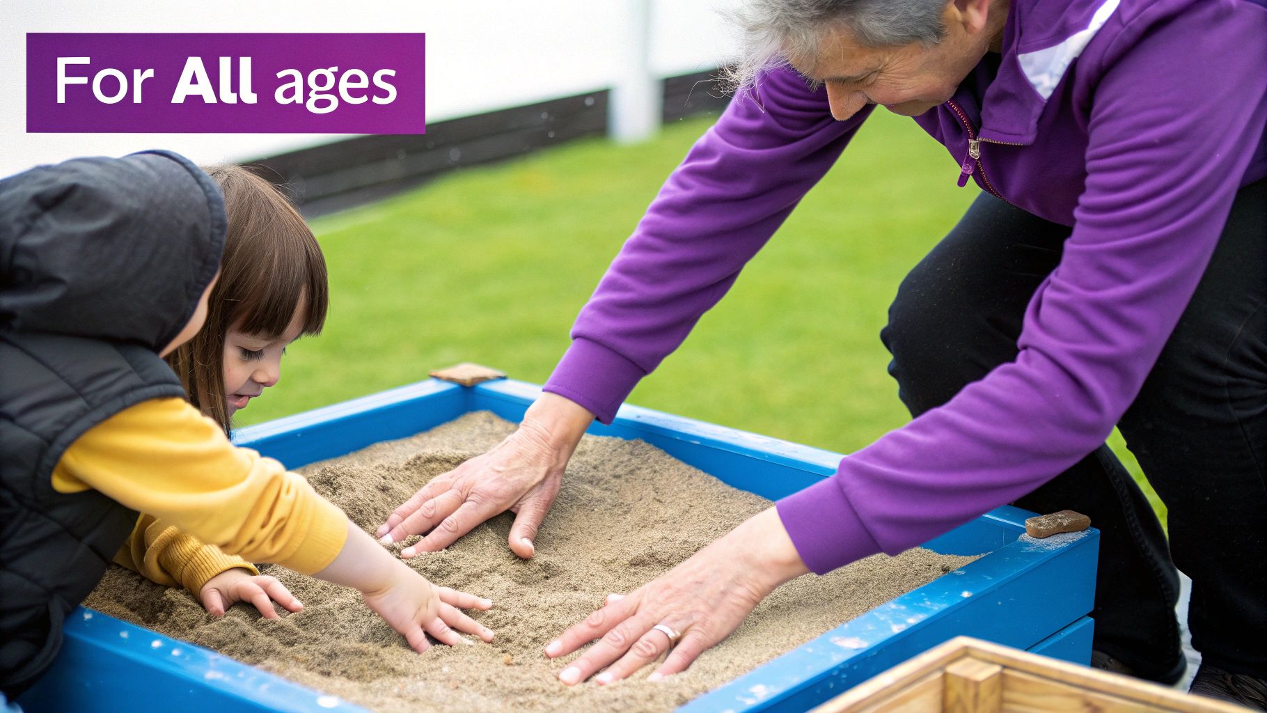 A multi-generational pair, an adult and a child, playing together in a blue sand tray, emphasizing inclusion 'For All ages'.