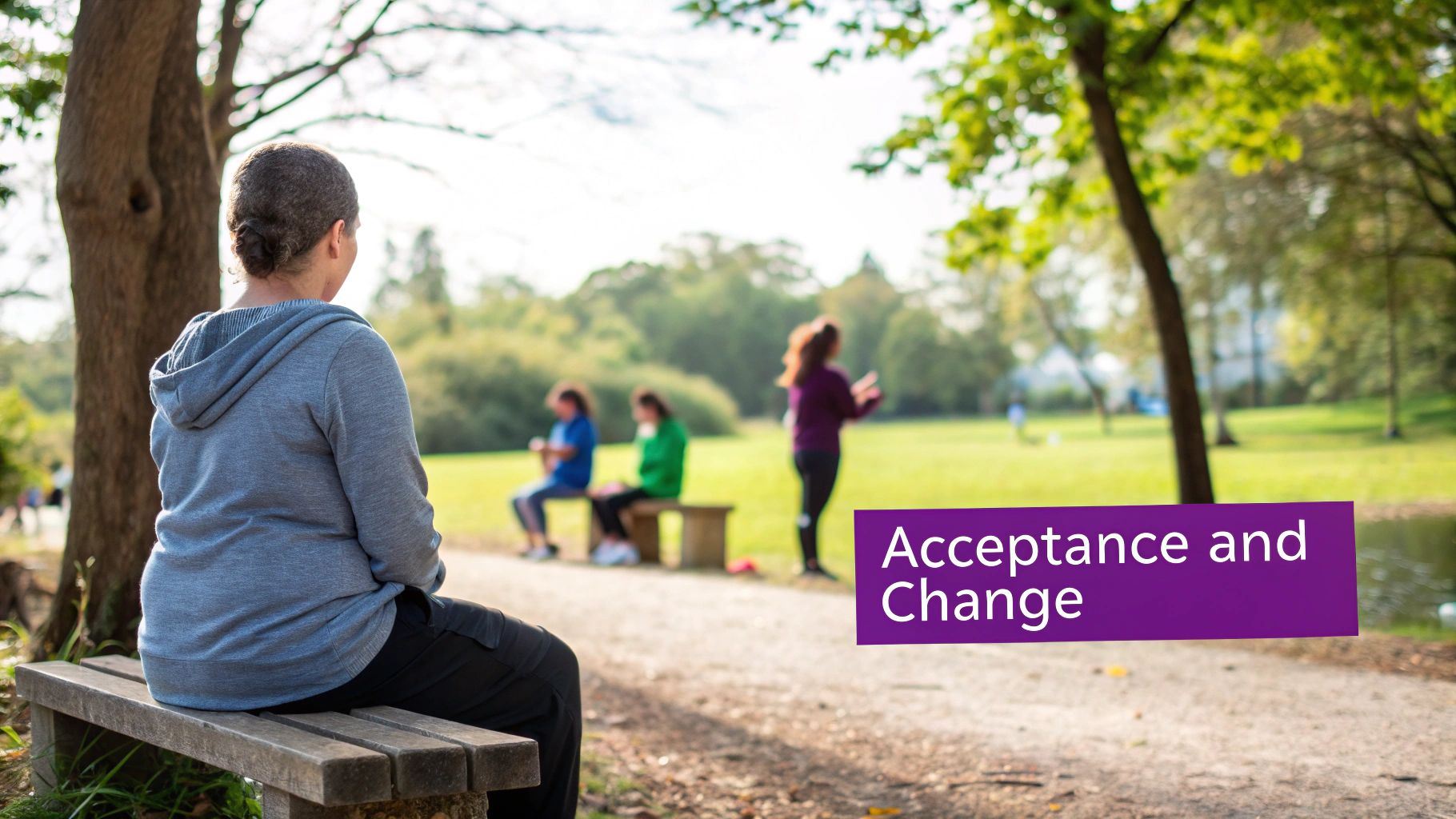 Back view of a woman in a grey hoodie sitting on a wooden bench in a sunny park.