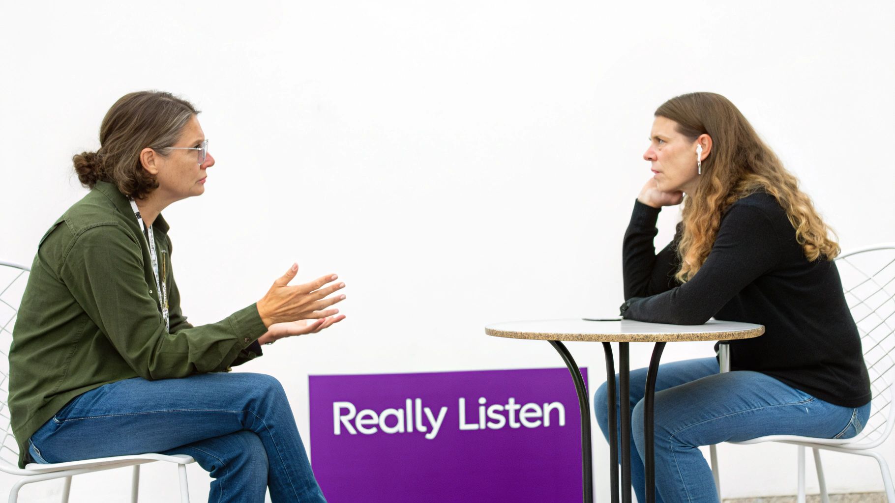 Two women conversing at a table, one gesturing while the other listens, with a "Really Listen" sign.