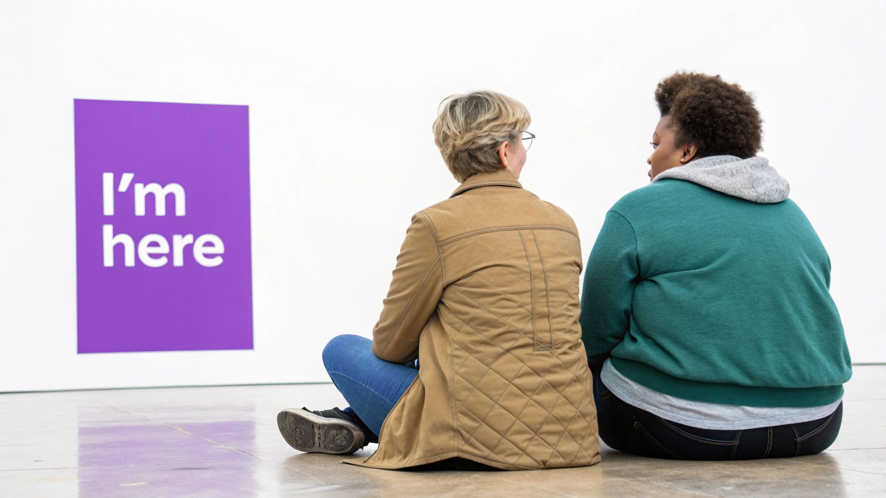 Back view of two individuals sitting on a floor, facing a purple sign with 'I'm here' text.