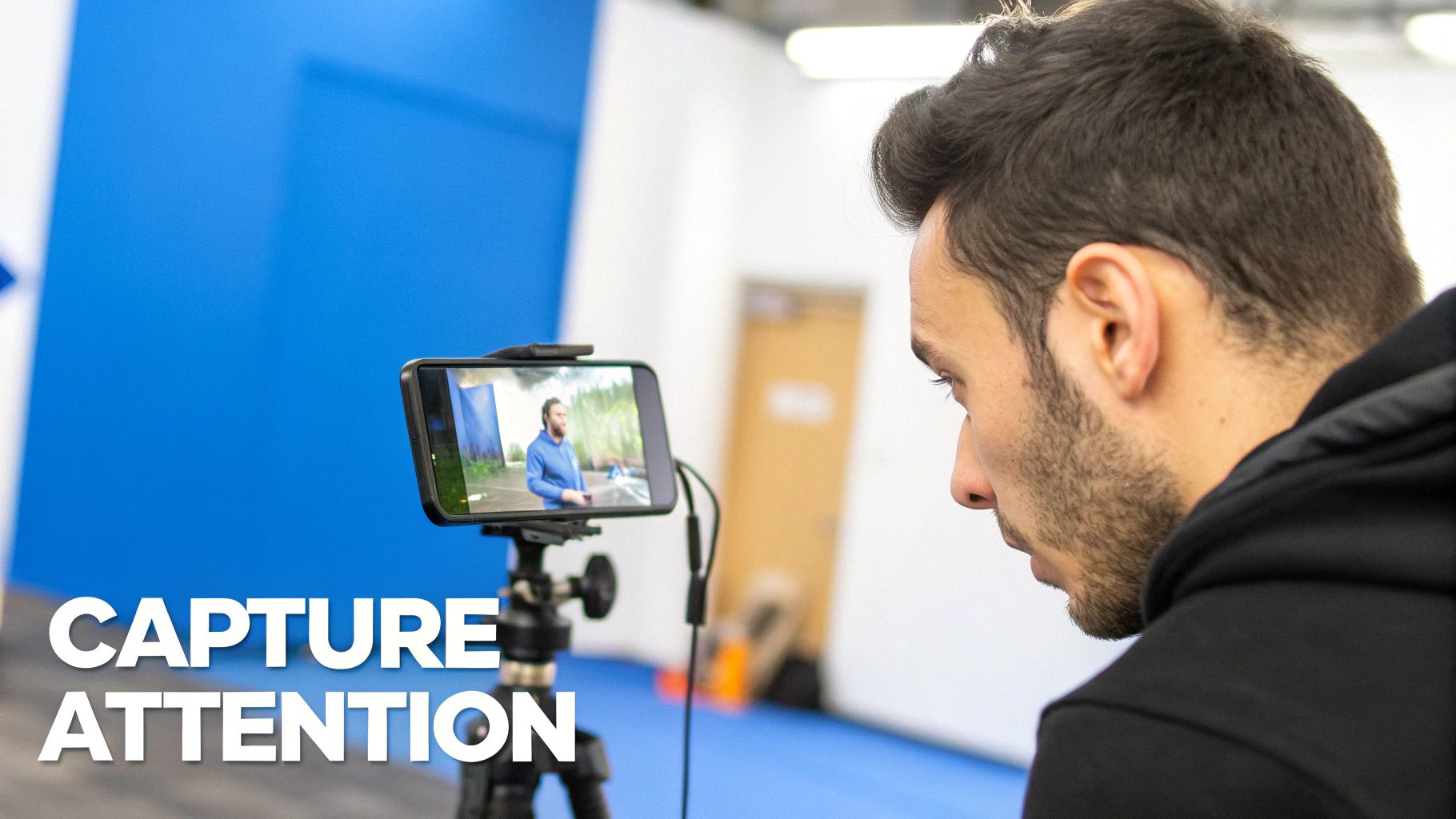A man observes a video recording on a smartphone, showing another man on screen with a blue background and text 'CAPTURE ATTENTION'.