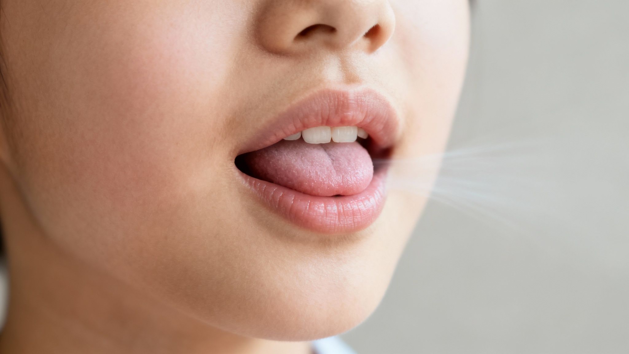 Close-up of a person's mouth with tongue extended, showing visible breath for pronunciation.
