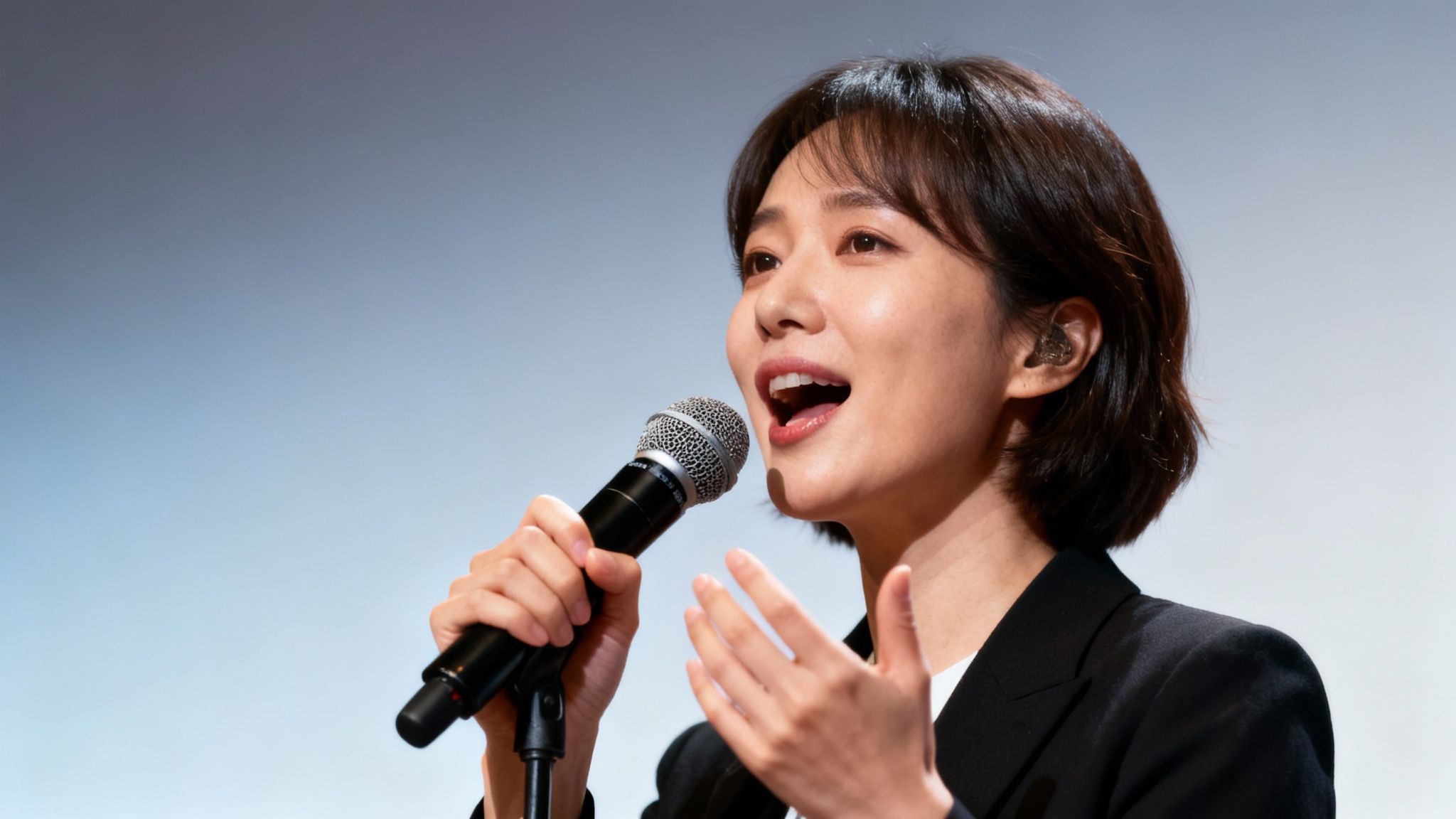 Close-up of a smiling Asian woman speaking passionately into a microphone while wearing an earpiece.