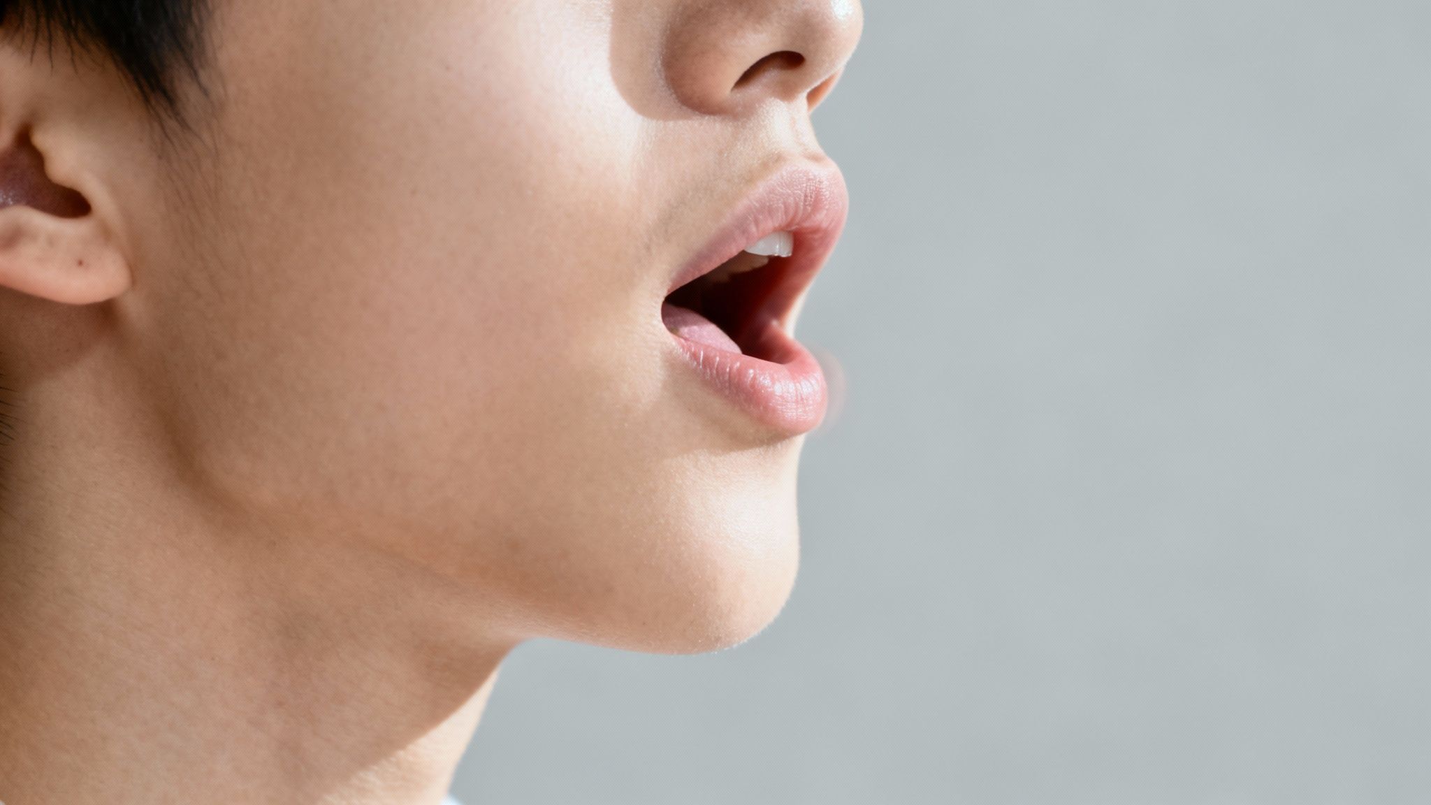 Close-up side profile of a person's open mouth, showing lips, teeth, and tongue.