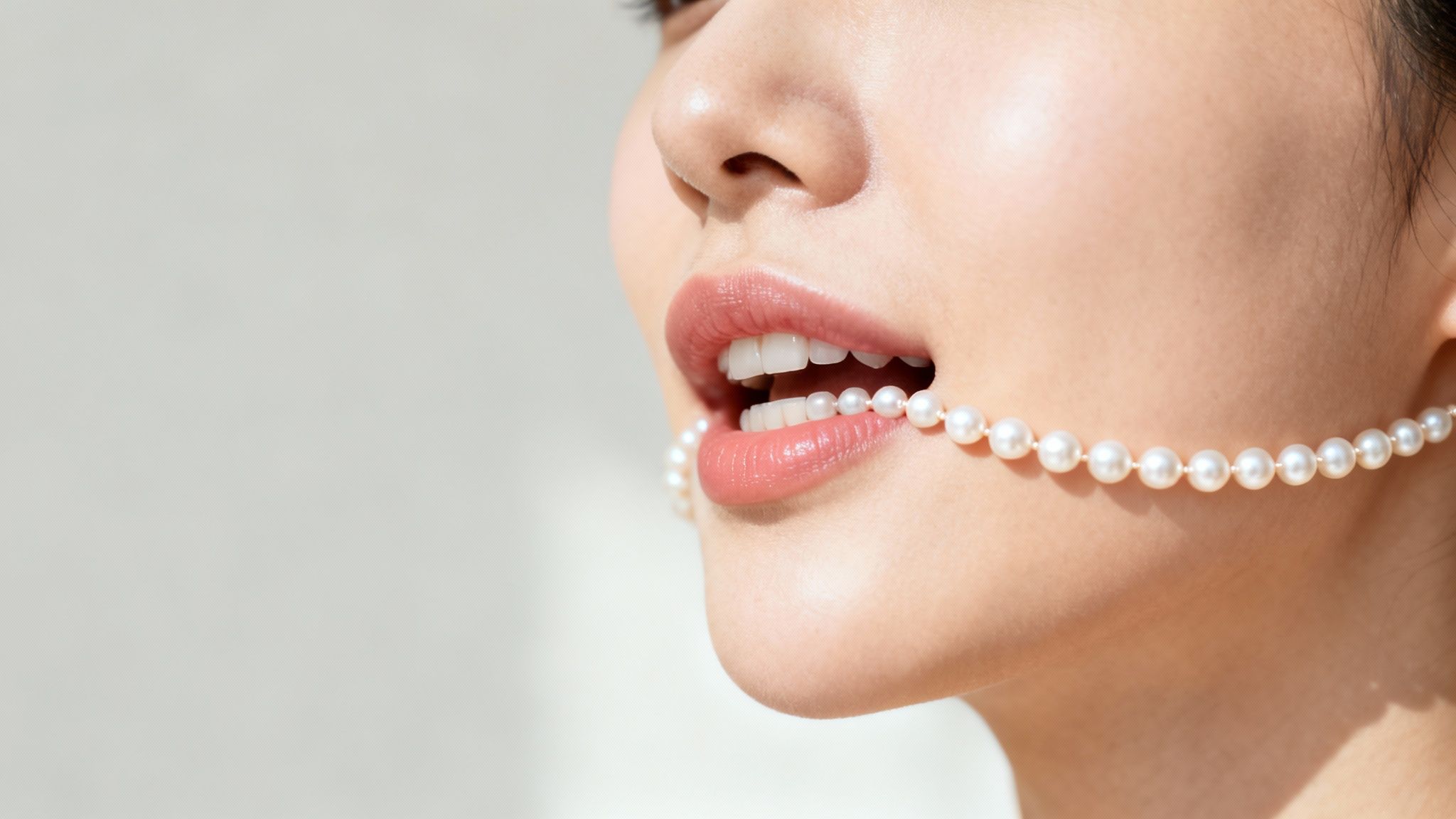Close-up of a woman's mouth holding a delicate strand of white pearls.