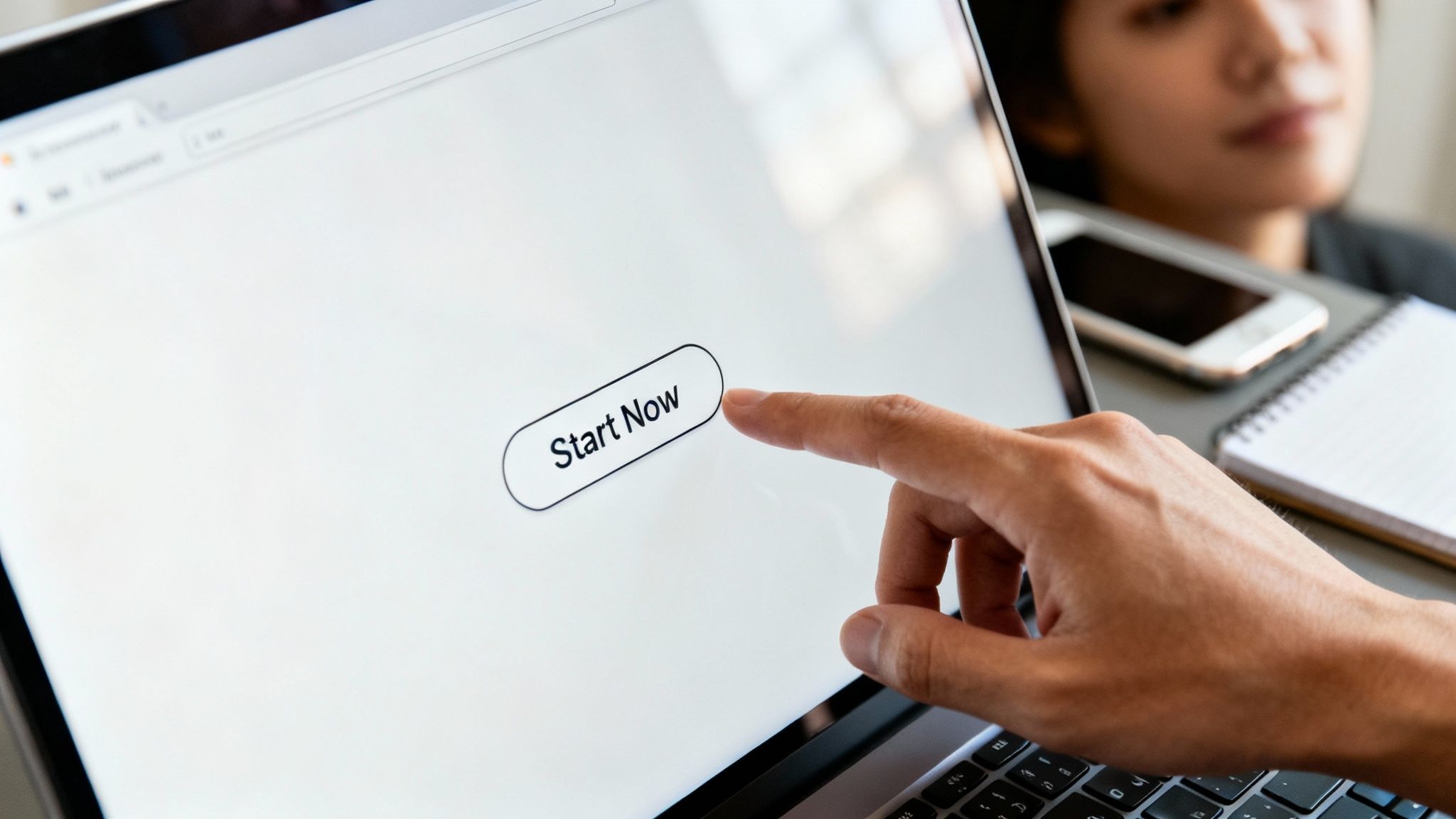 A person's finger taps a 'Start Now' button on a laptop screen, ready to begin.