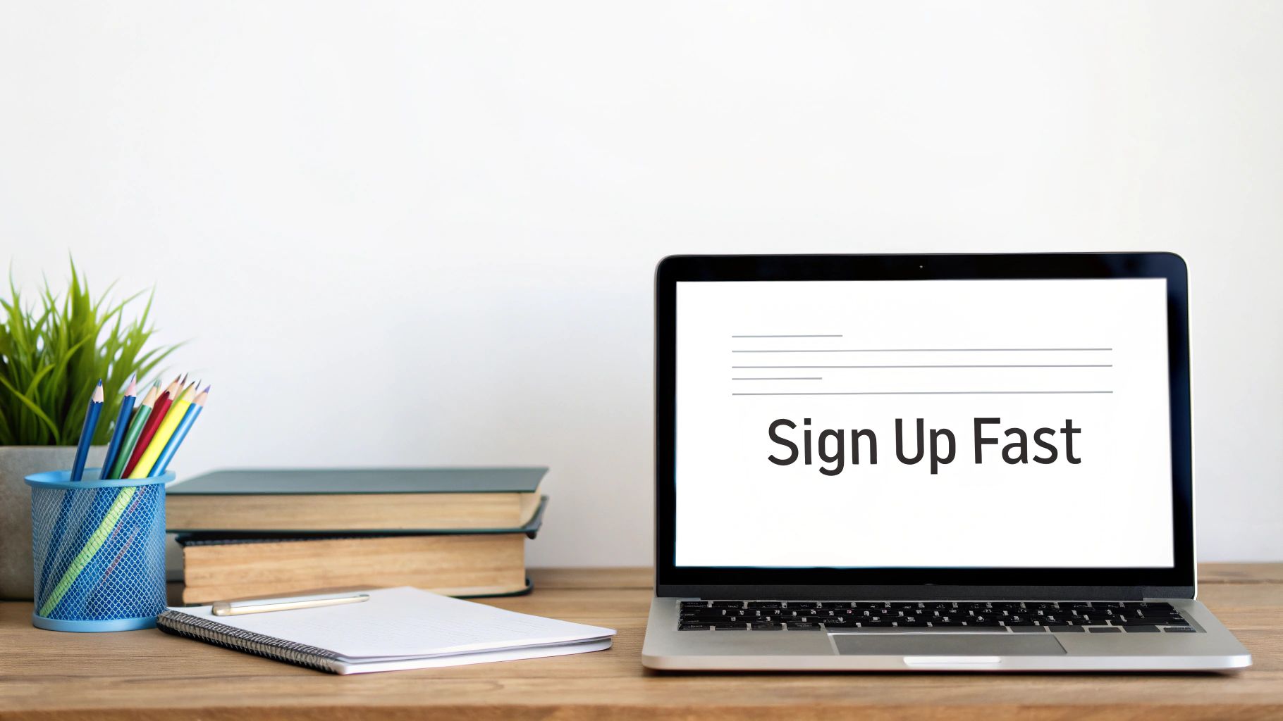 A wooden desk with a laptop displaying 'Sign Up Fast', books, colorful pencils, and a plant.