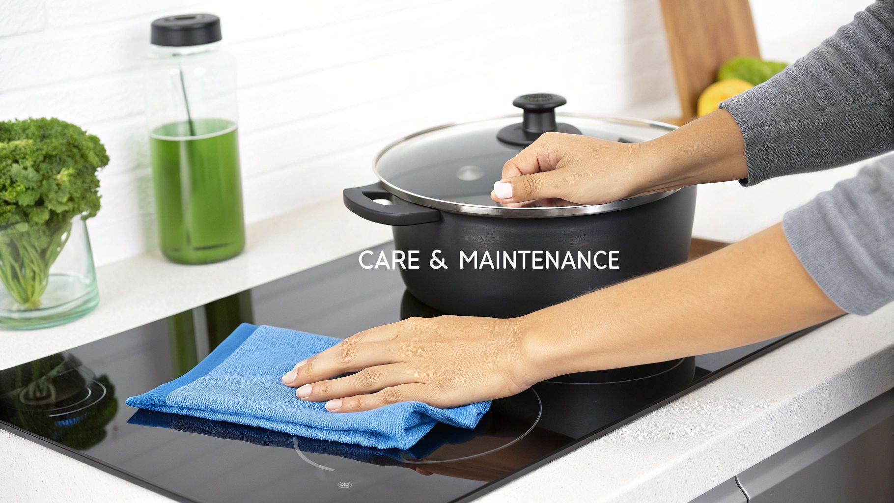 A person is carefully cleaning a black induction cooktop with a blue microfiber cloth, with a pot on it.