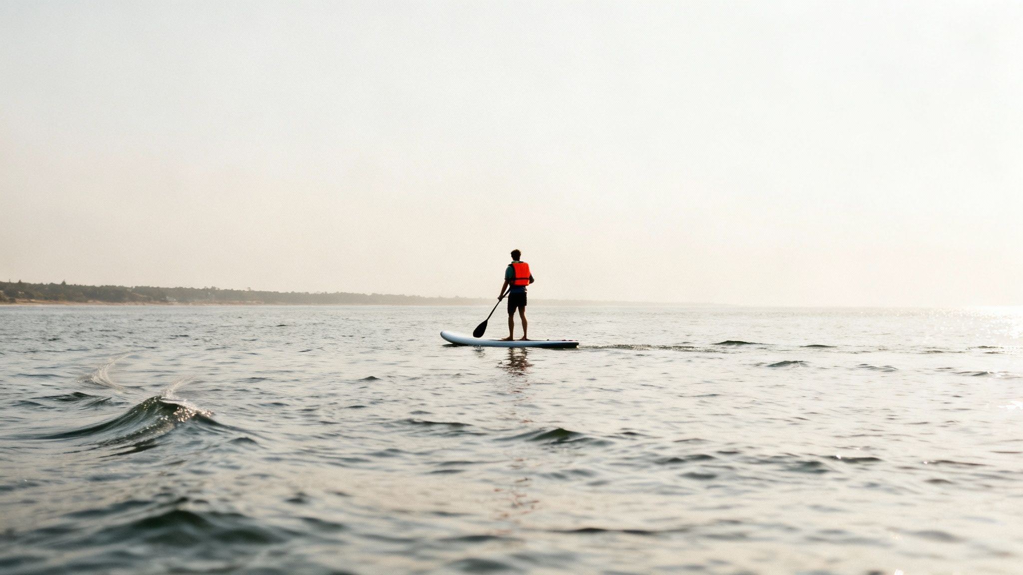 A paddleboarder on the water as the sun sets, illustrating potential offshore wind conditions.