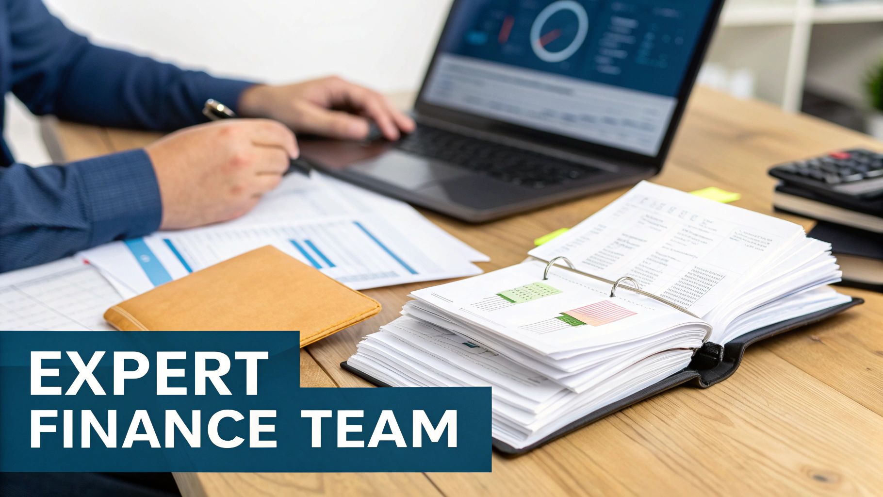 A person working on financial reports with a laptop, papers, and an open binder on a wooden desk.