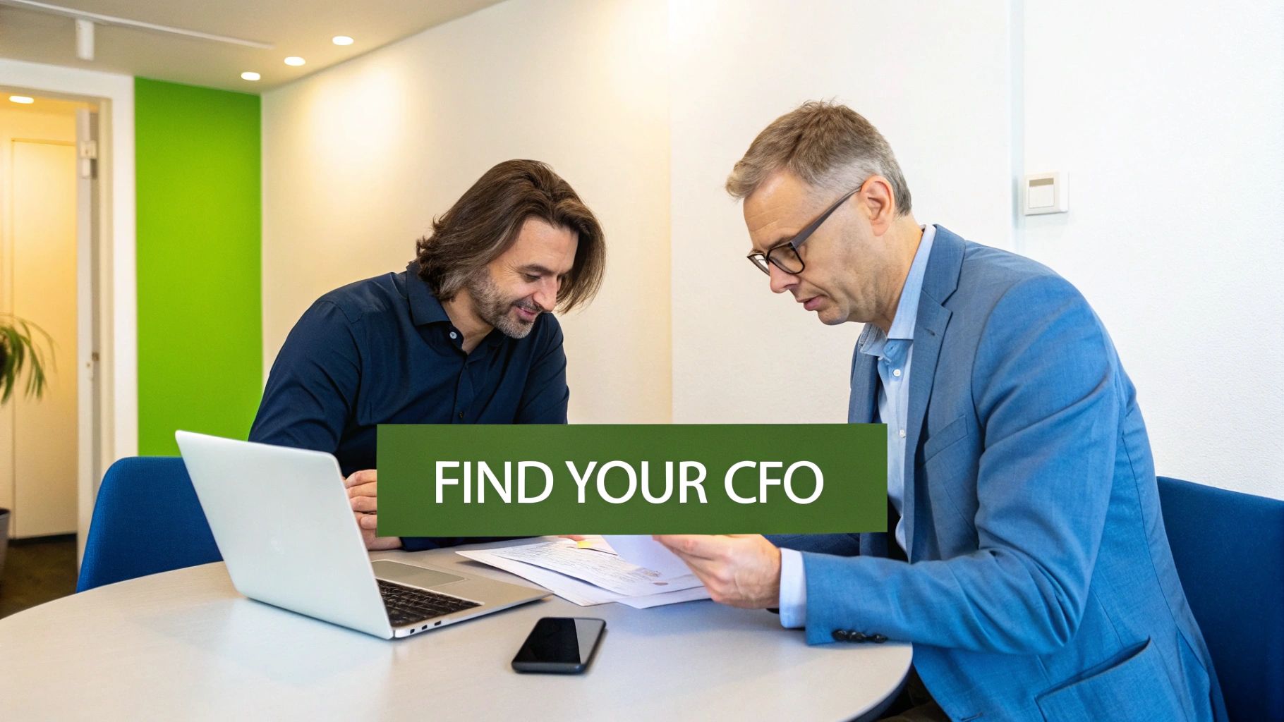 Two businessmen collaborate in an office, reviewing documents and using a laptop on a table.