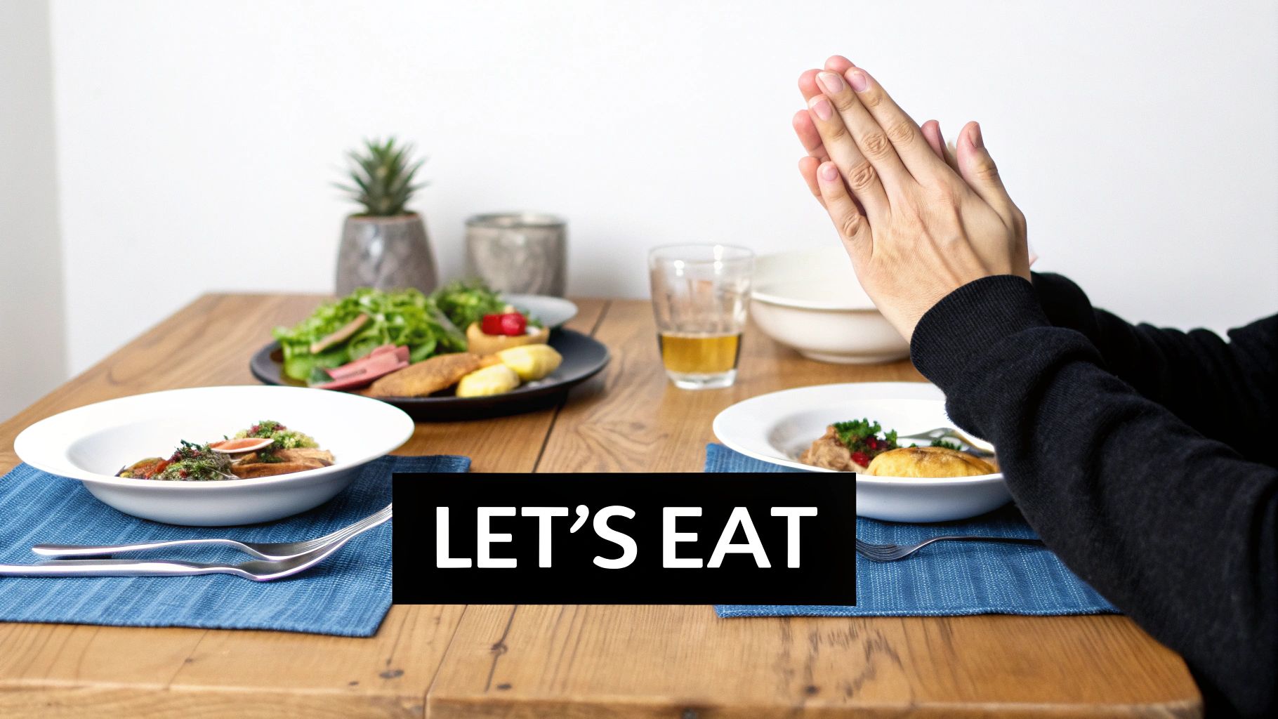 A person with hands clasped in prayer before a meal set with two plates of food and drinks.