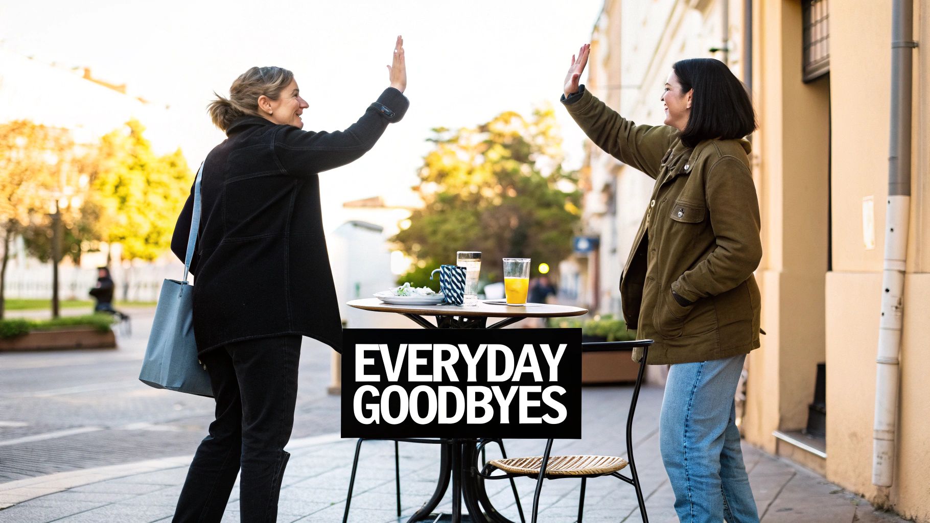 Two smiling women high-fiving at an outdoor cafe, with a sign reading 'EVERYDAY GOODBYES'.