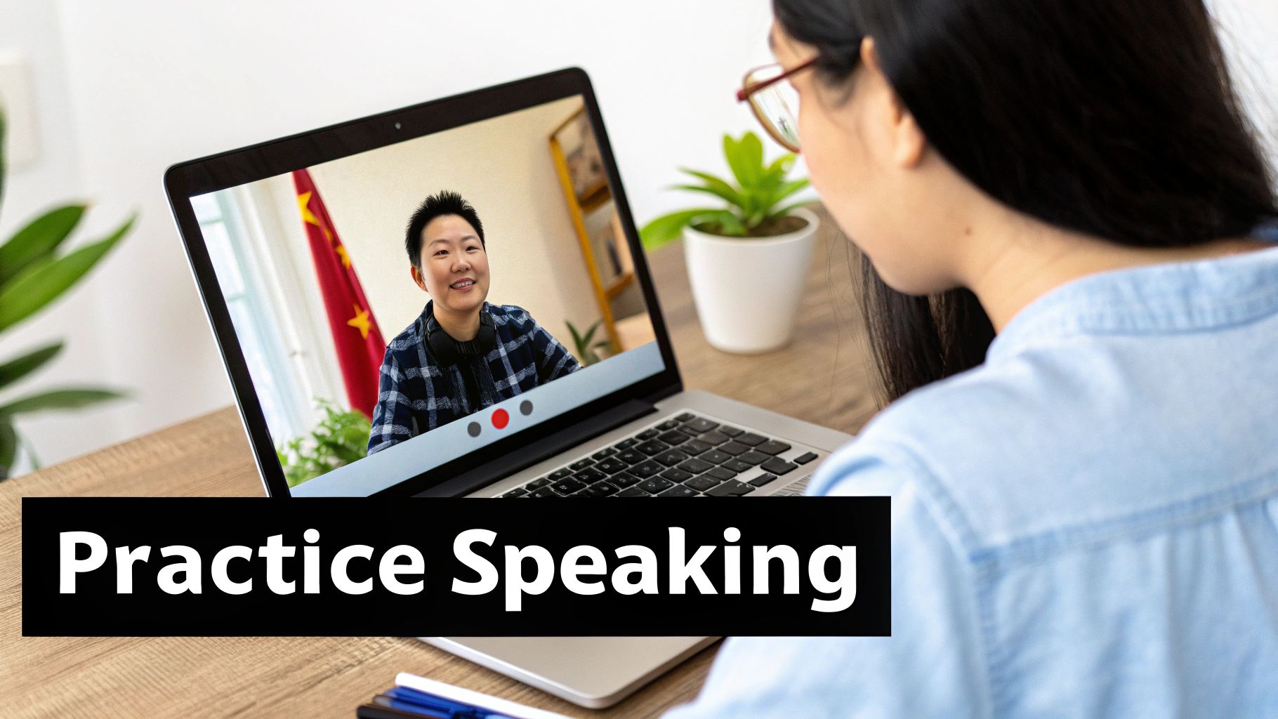 A person practices speaking on a video call with a Chinese teacher, laptop on a wooden desk.