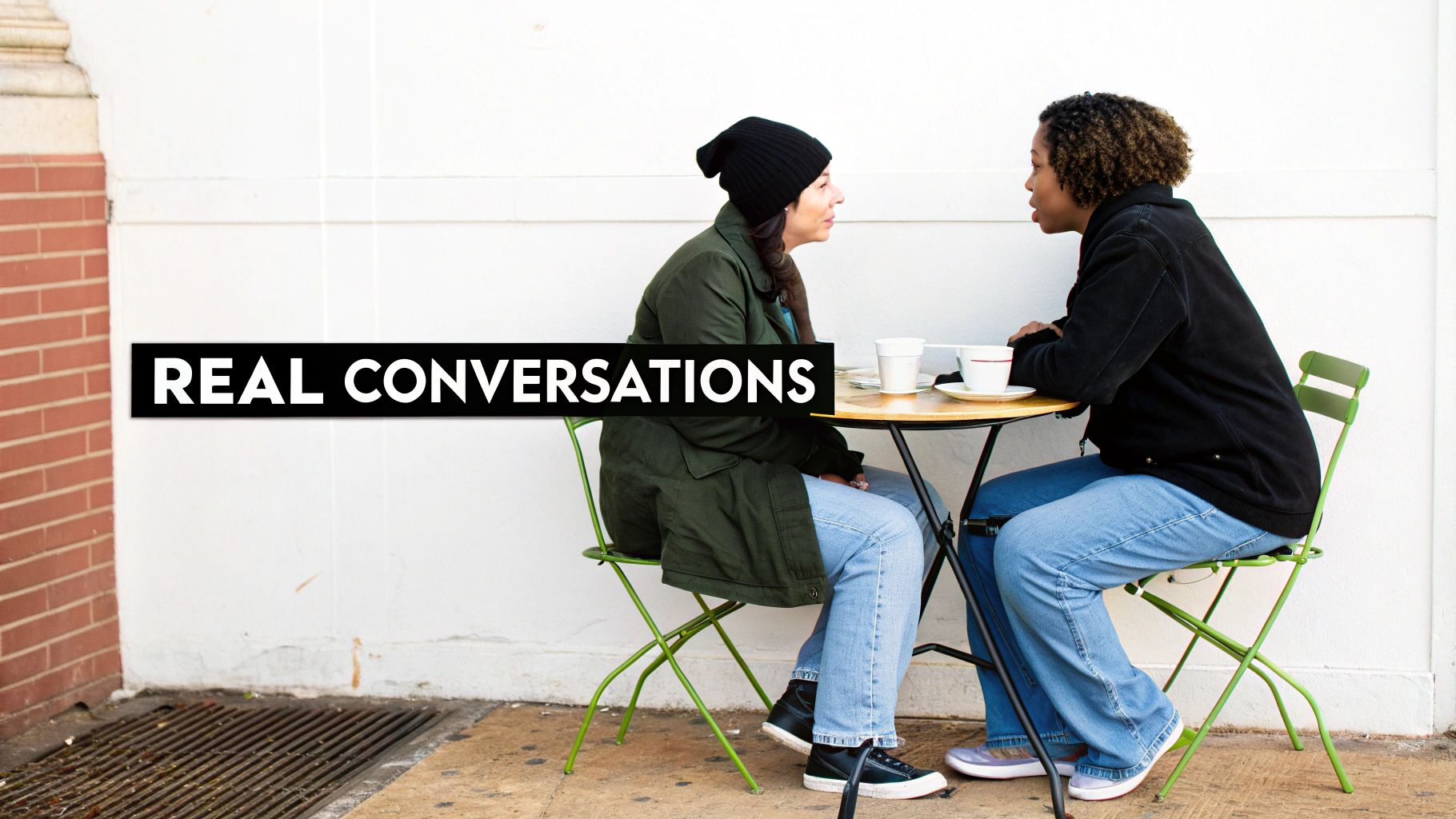 Two women at an outdoor cafe table with coffee, engaged in 'REAL CONVERSATIONS'.