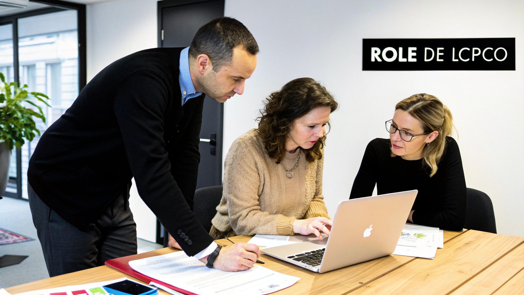 Trois collègues collaborent en réunion, examinant des documents et un ordinateur portable, avec un signe de rôle en arrière-plan.