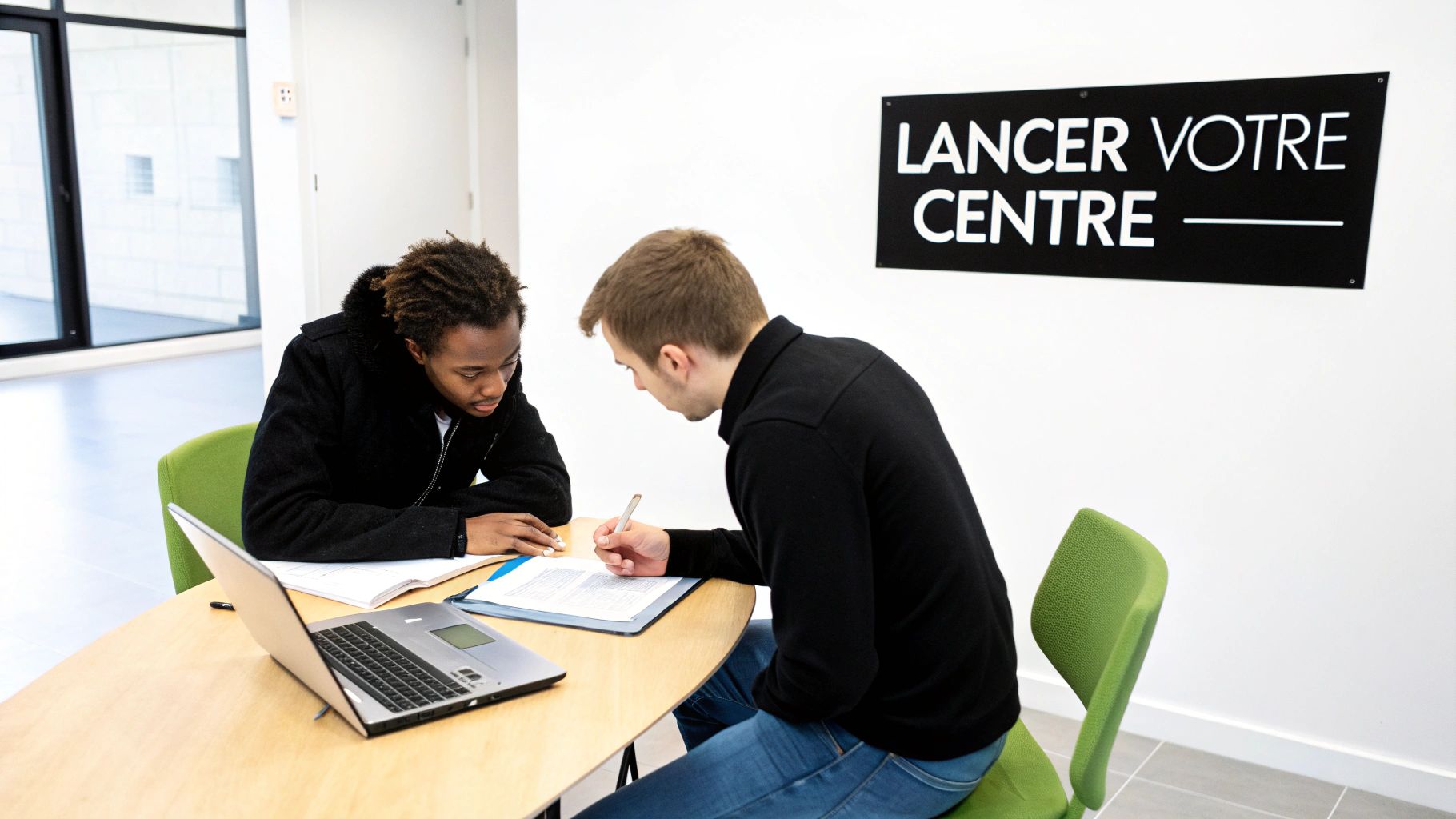 Deux hommes à une table, travaillant sur des documents et un ordinateur portable, avec l'enseigne "Lancer votre centre" en arrière-plan.